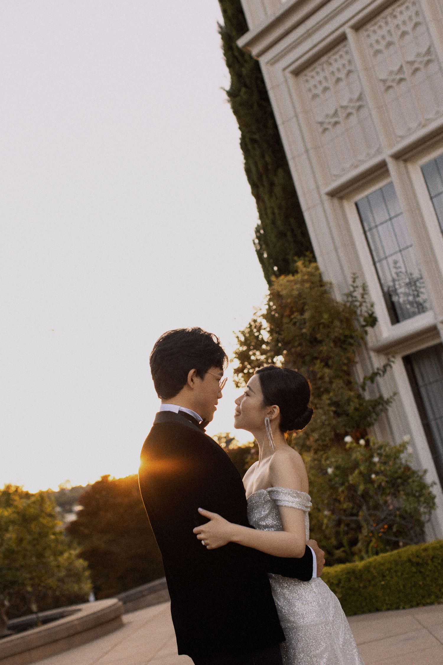 A romantic embrace between newlyweds outside a grand building during golden hour sunset.