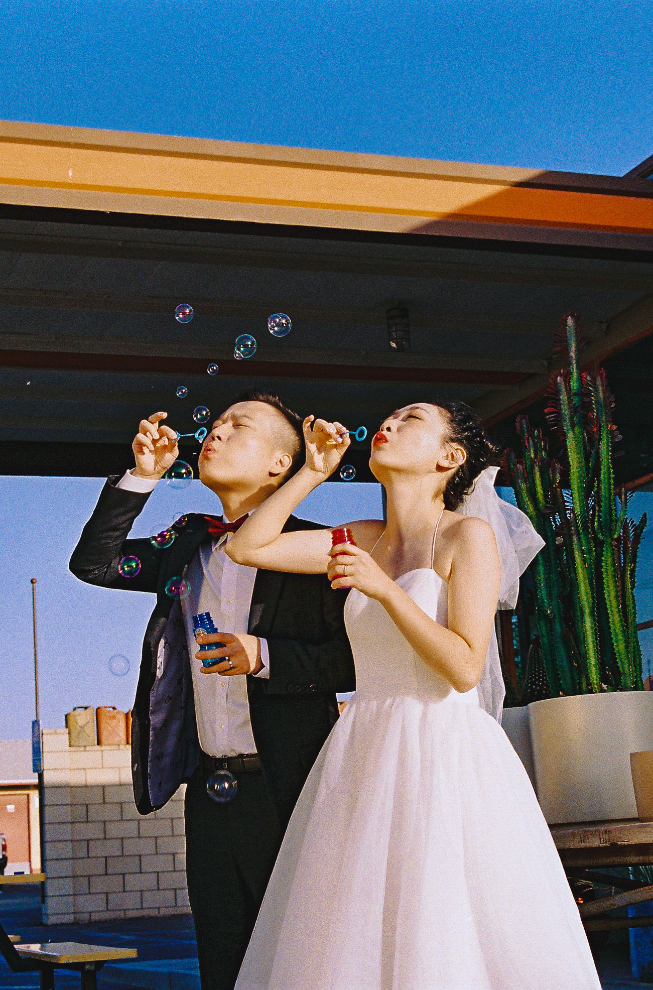 A playful wedding couple blowing bubbles together at an outdoor reception.