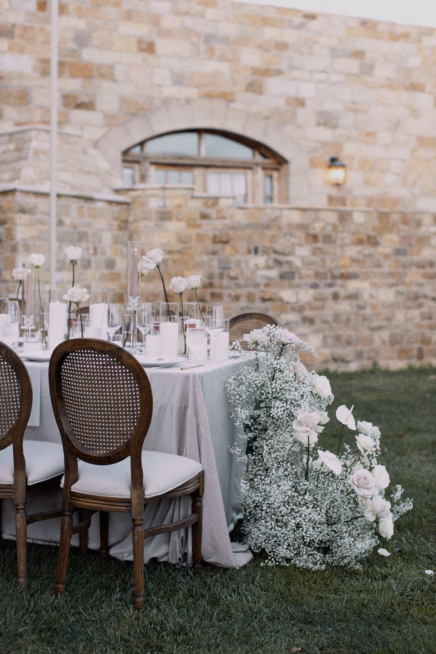White floral centerpieces and elegant table settings against a rustic stone wall backdrop.