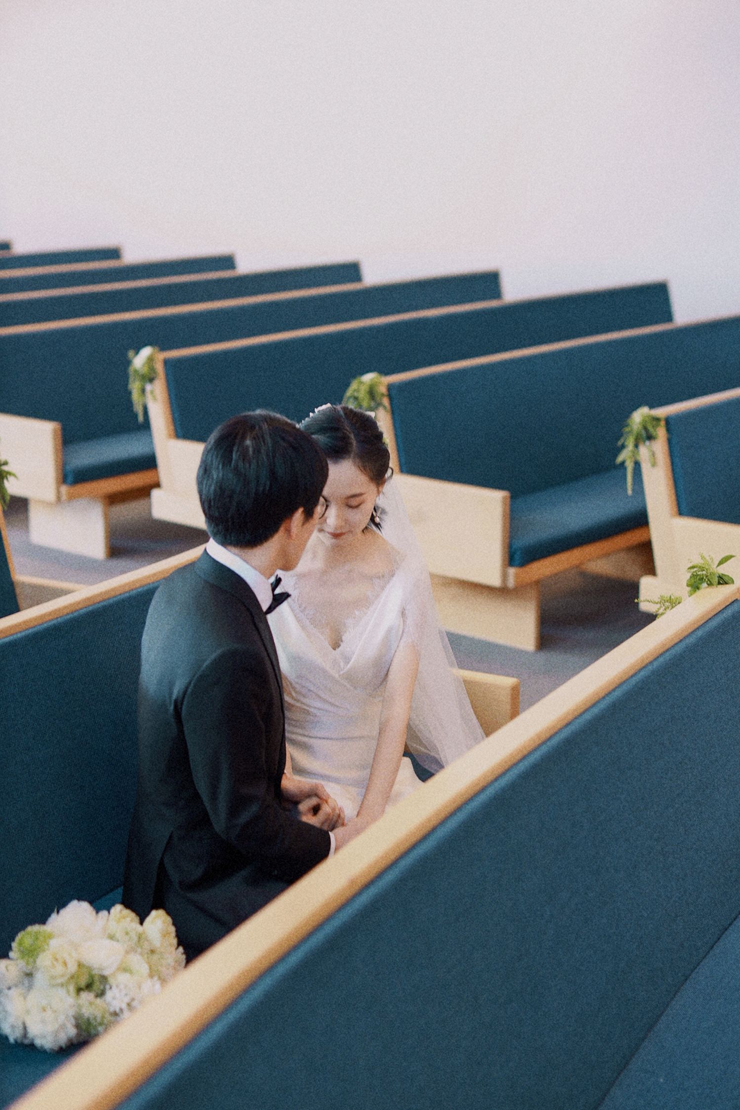A wedding couple shares an intimate moment in church pews decorated with floral accents.