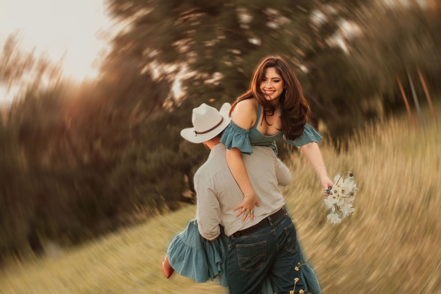 Couple embraces in golden field at sunset as partner lifts and spins while flower bouquet flies through the air.