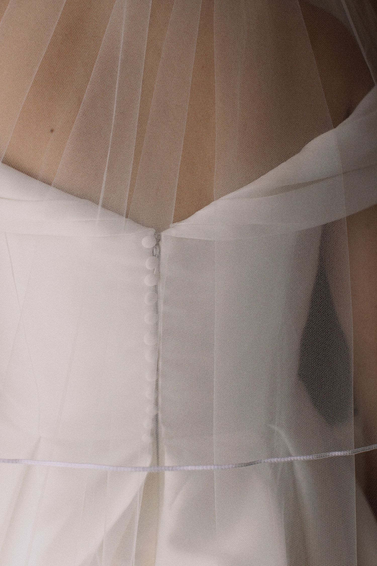 Close-up detail of white wedding dress buttons and delicate veil.