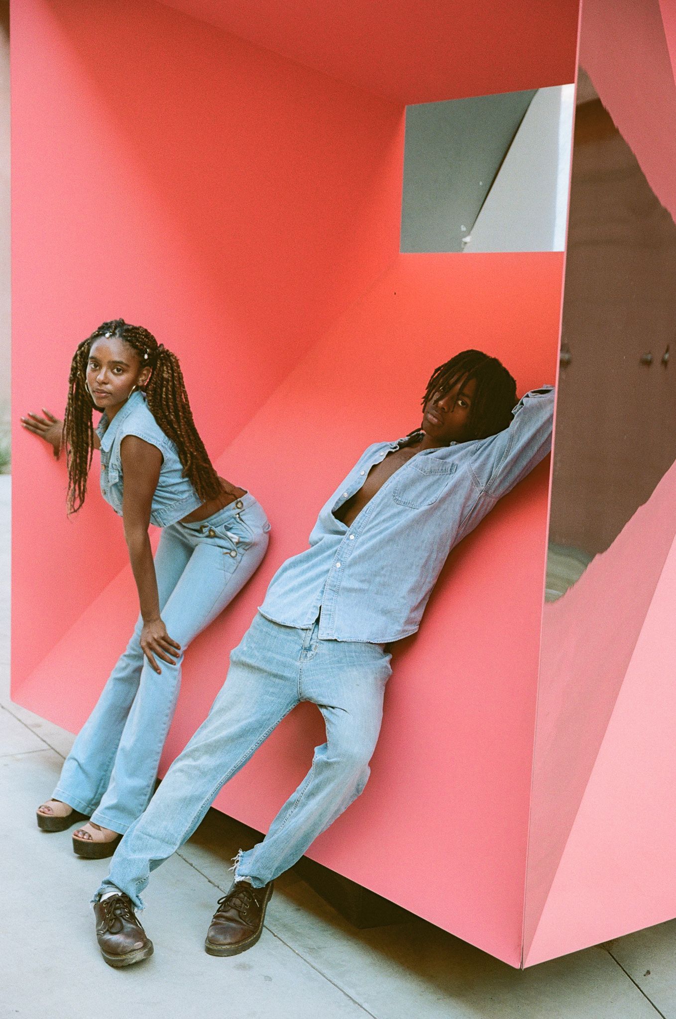 Fashion models posing against geometric pink wall wearing light denim and casual wear in artistic composition.