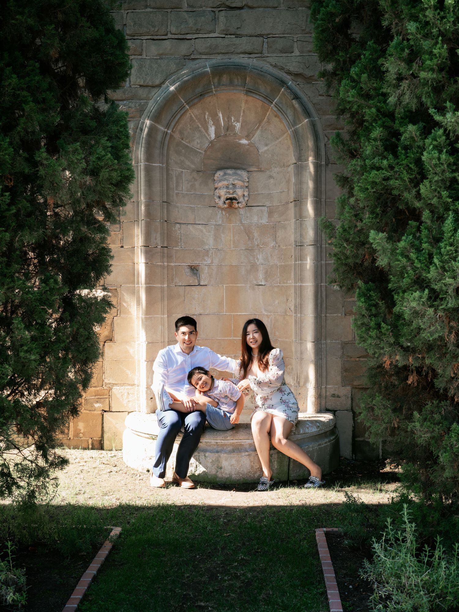 A family sitting together on a stone bench under an arched alcove framed by greenery.