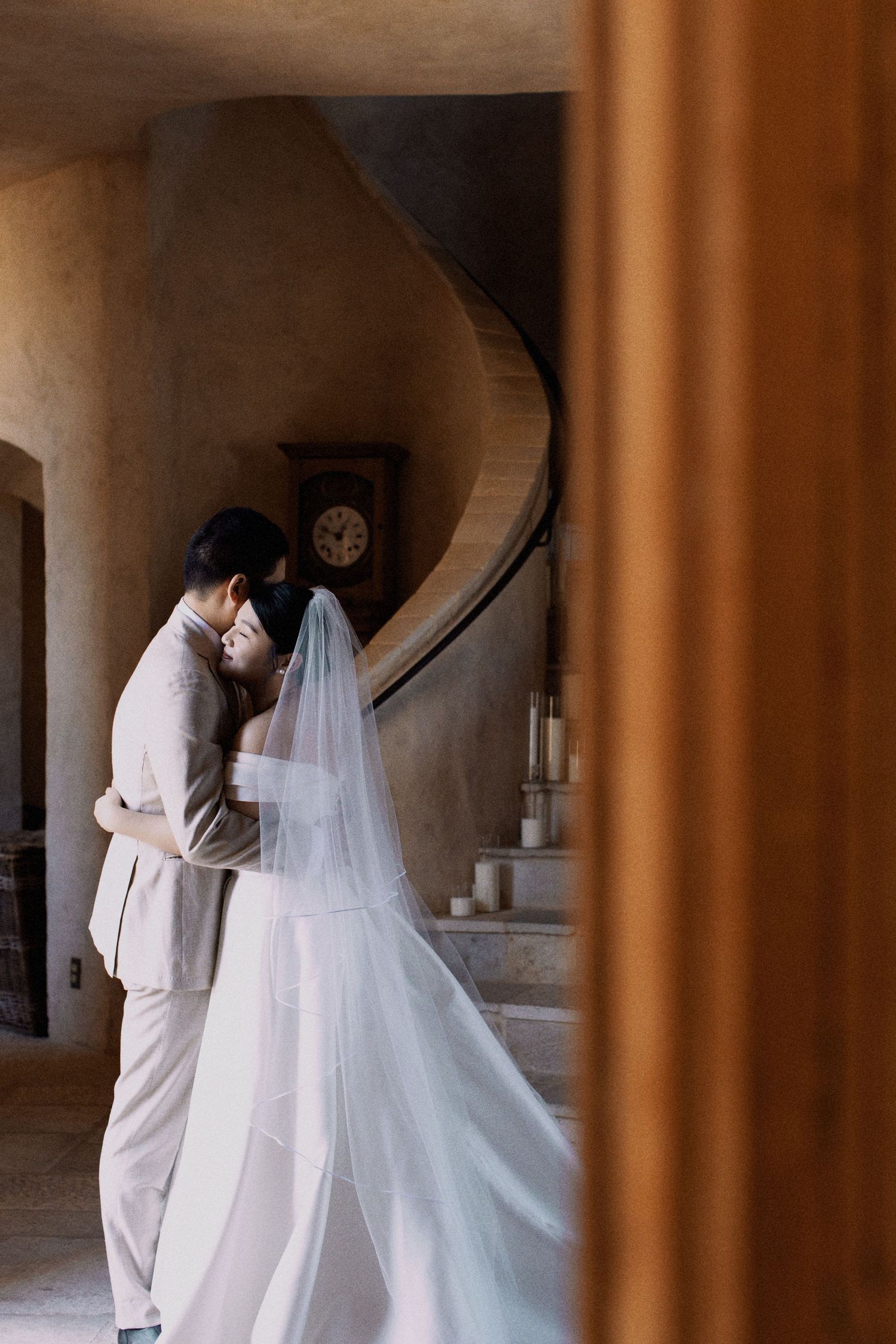 A romantic moment between newlyweds near a spiral staircase in soft window light.
