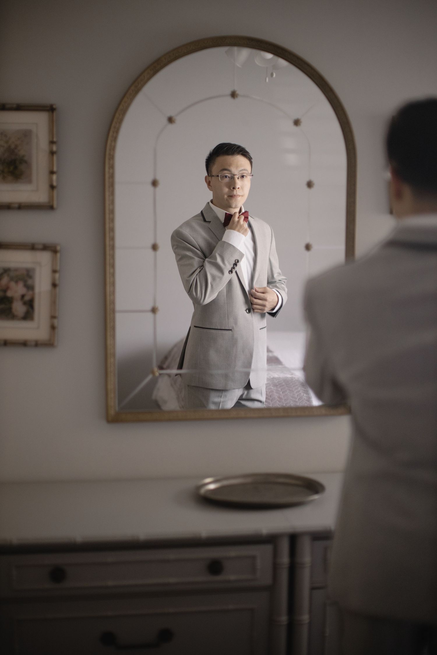 Reflection in an arched mirror shows someone adjusting a formal grey suit.