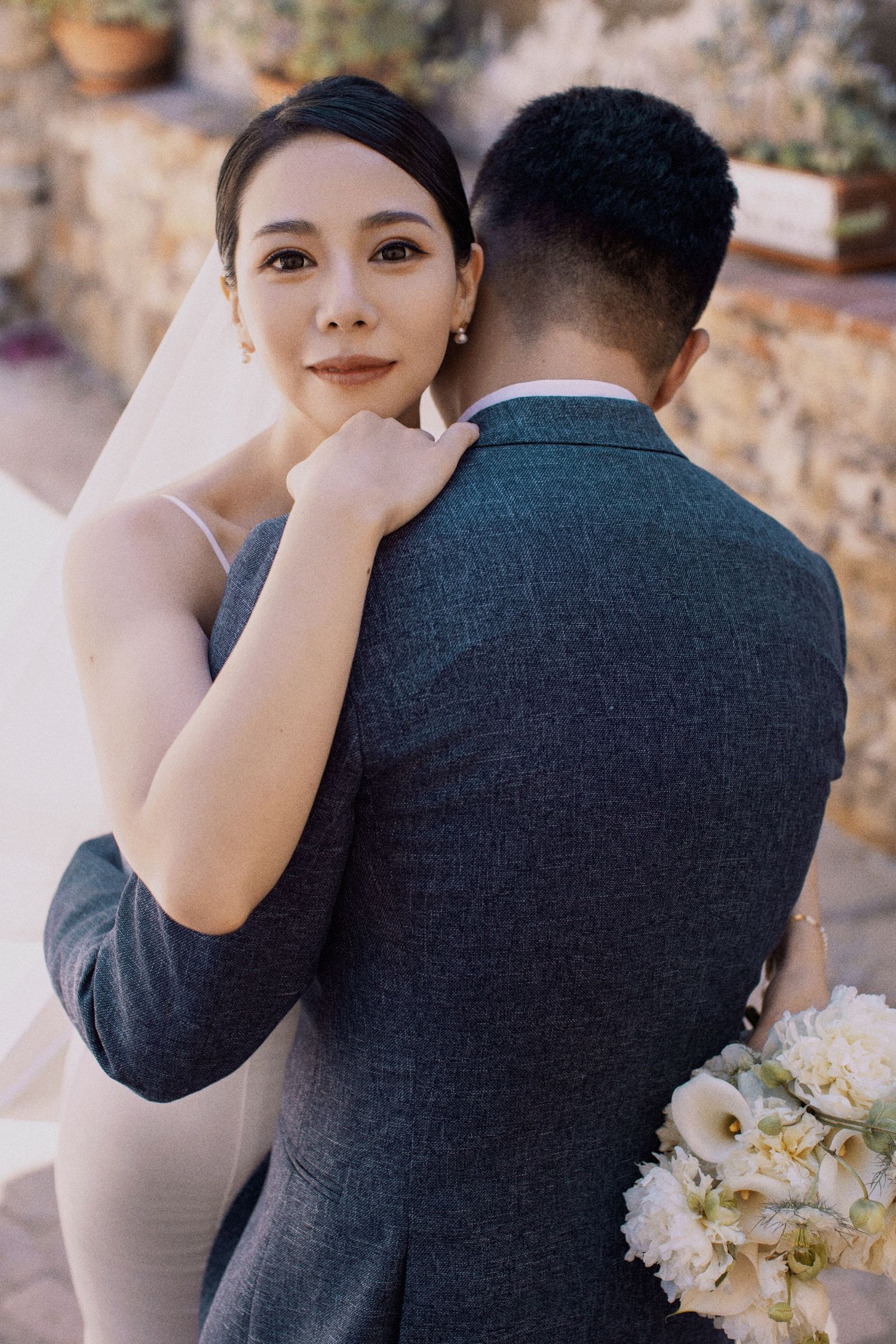 Romantic wedding portrait of couple embracing near stone wall.