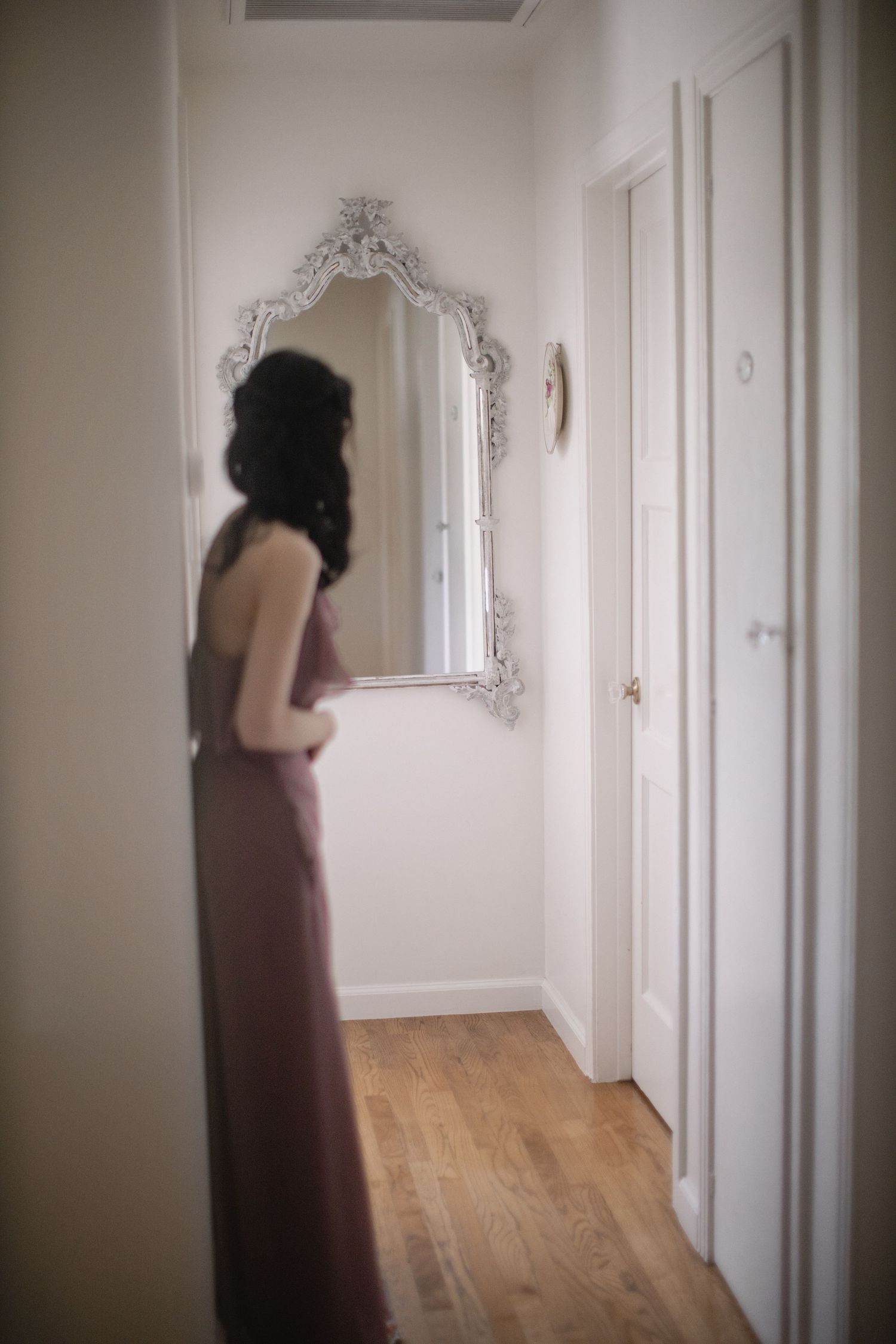 Ornate vintage mirror hangs on white wall beside wooden door in hallway.