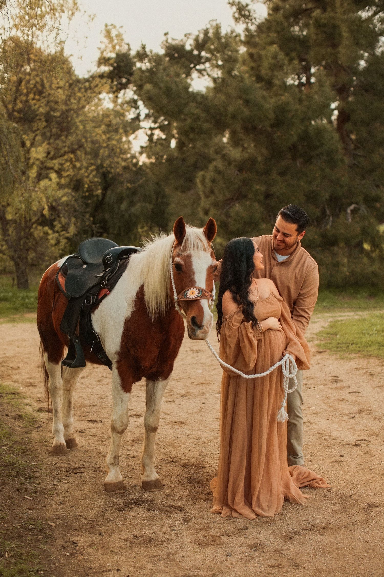 A painted pony with saddle stands beside a couple in romantic autumn scene on a dirt path.