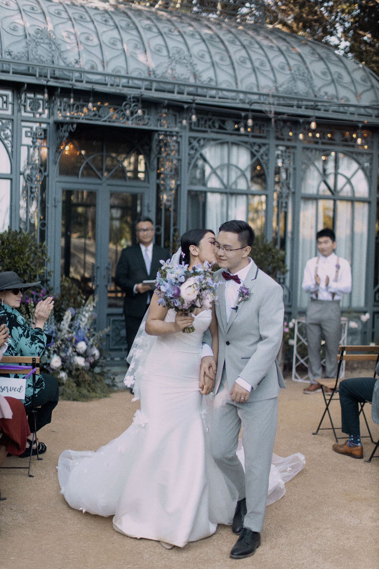 Wedding celebration outside a glass conservatory with elegant floral decorations.