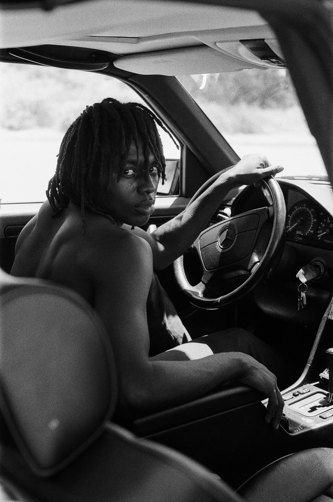 Black and white photo of someone driving a car, viewed from the back seat.