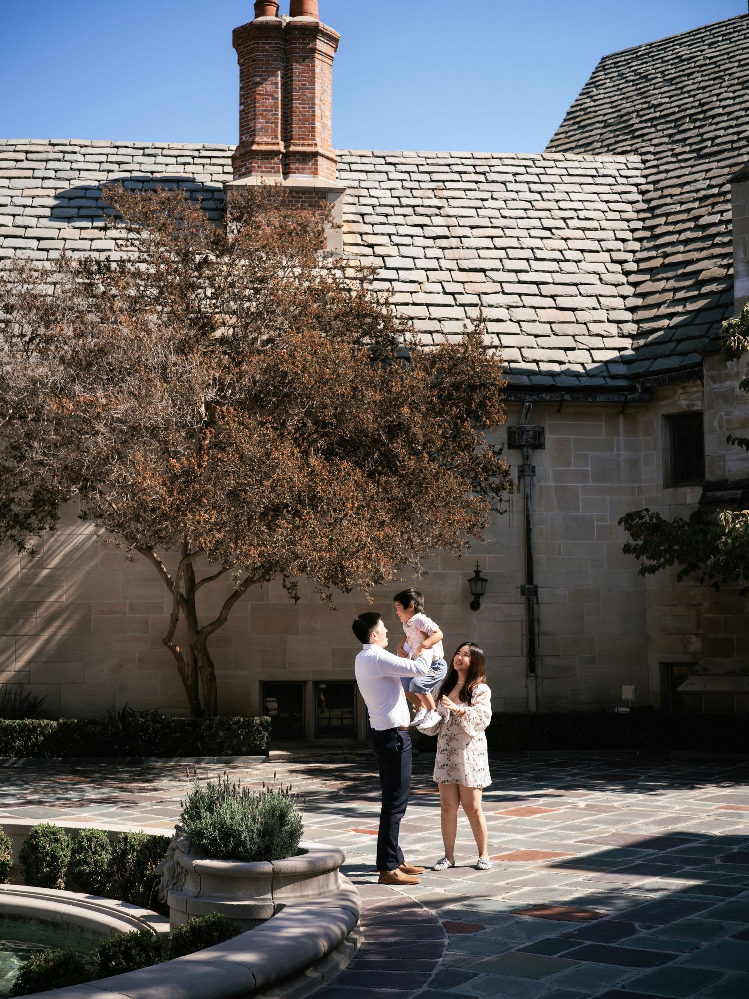 Family standing together on stone patio near historic building with brick chimney.
