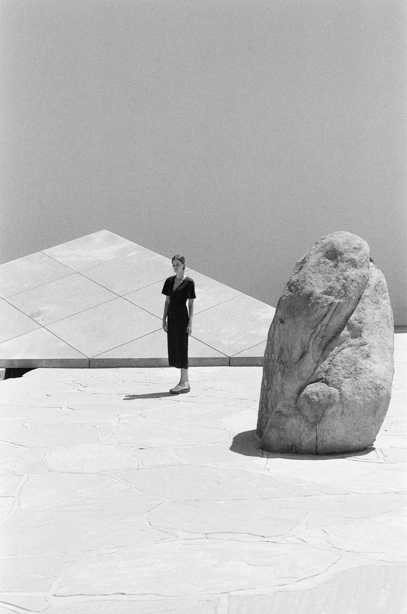 Artistic black and white composition with figure and stone sculpture on geometric surface.