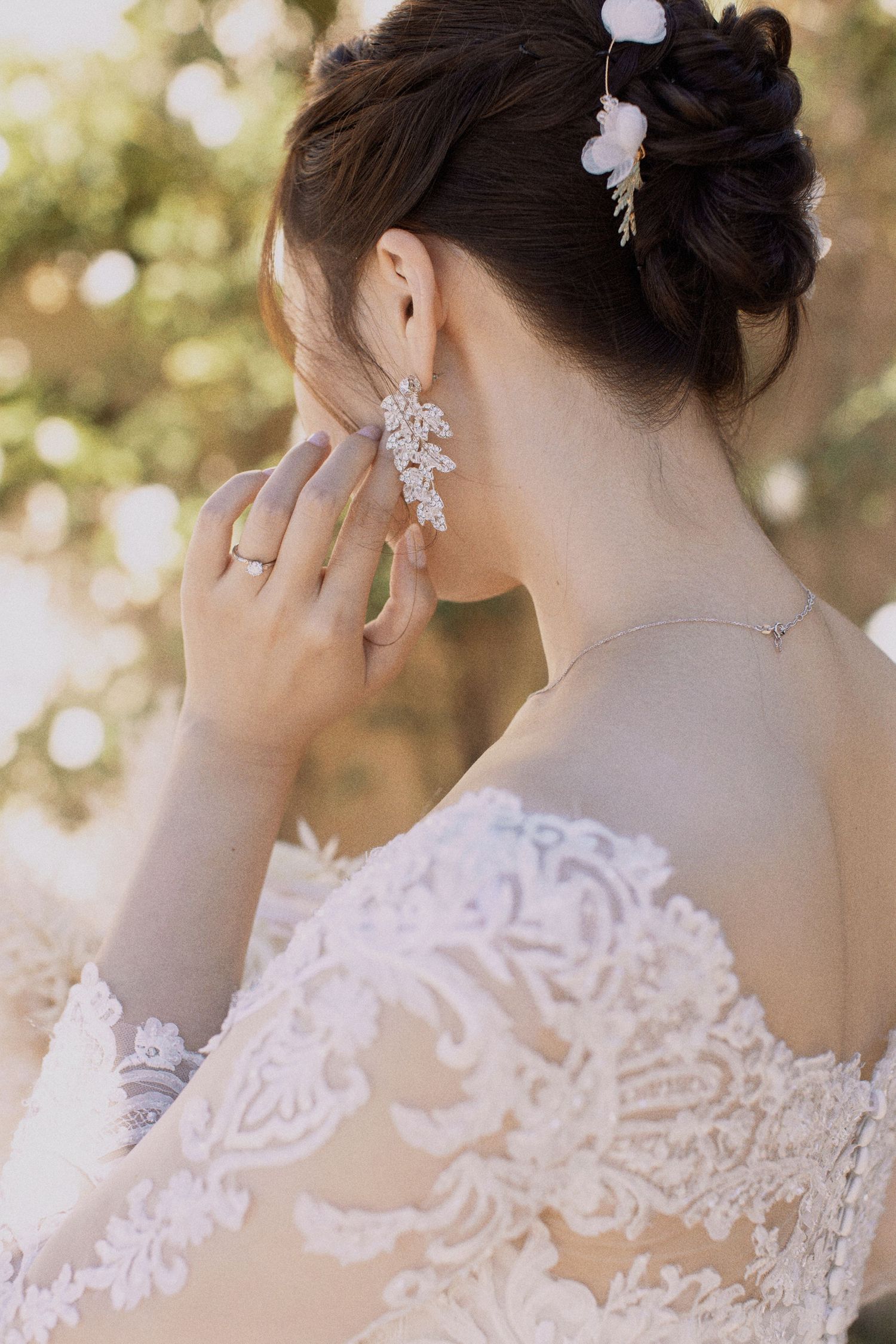 Close-up of bride's updo hairstyle with crystal earrings and delicate lace dress details.