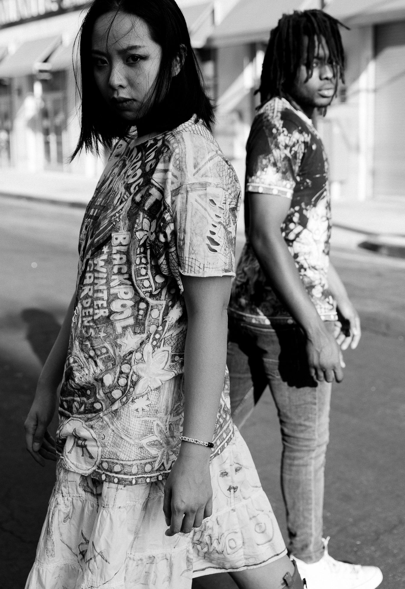 Black and white portrait of two models in streetwear on urban sidewalk.