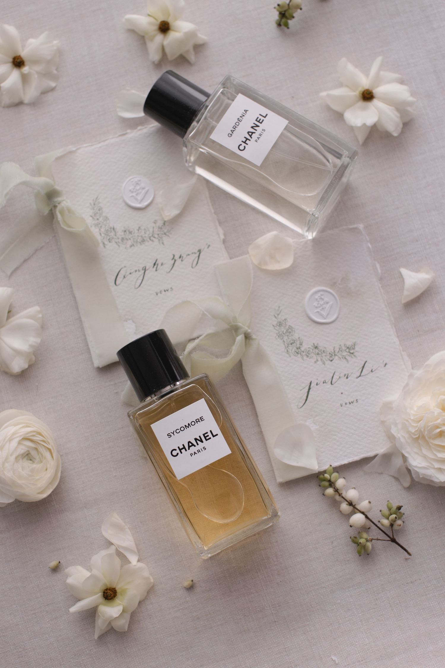Chanel perfume bottles styled with white flowers and wedding stationery on light background.