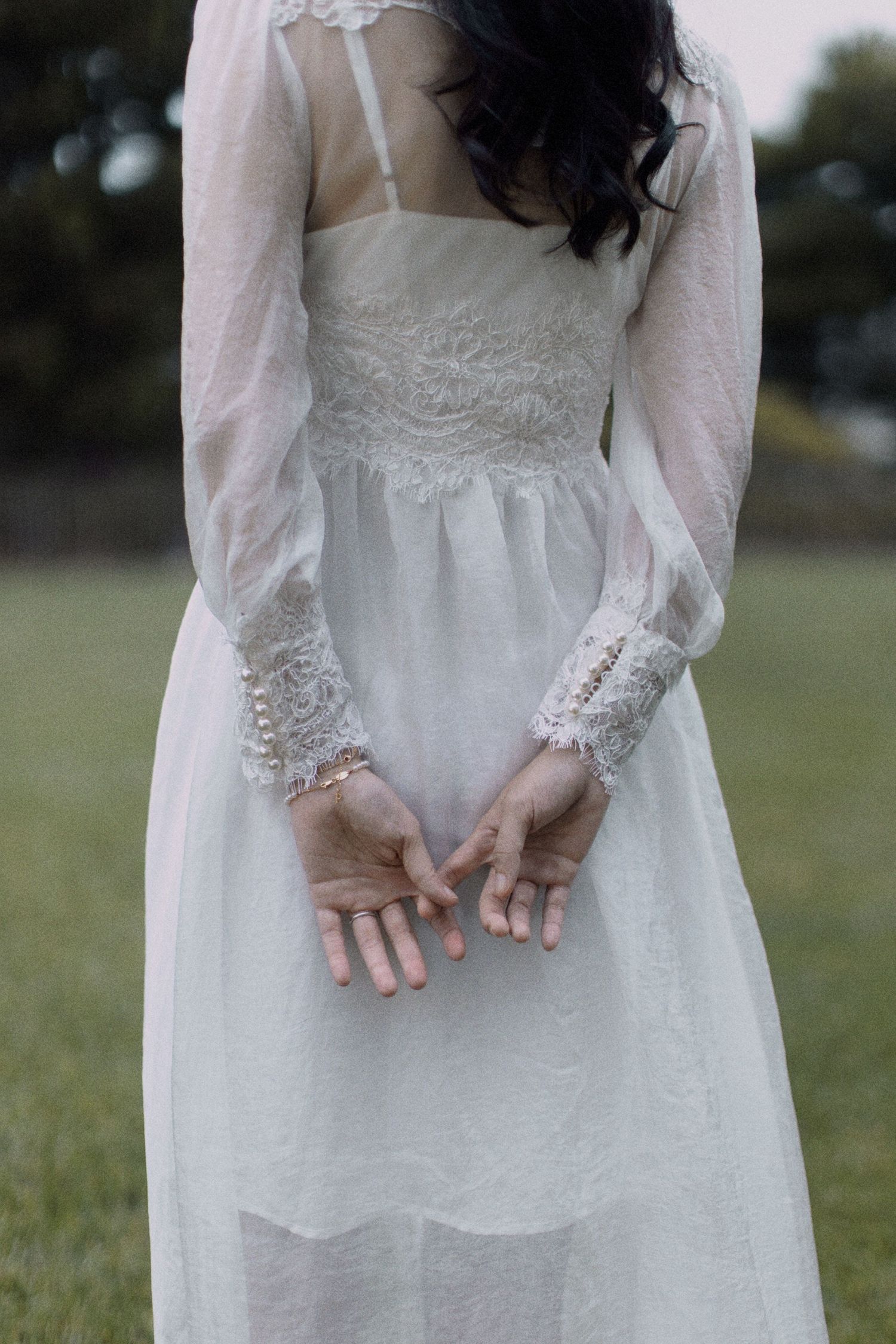 Back view of a white lace wedding dress with sheer long sleeves in a garden setting.