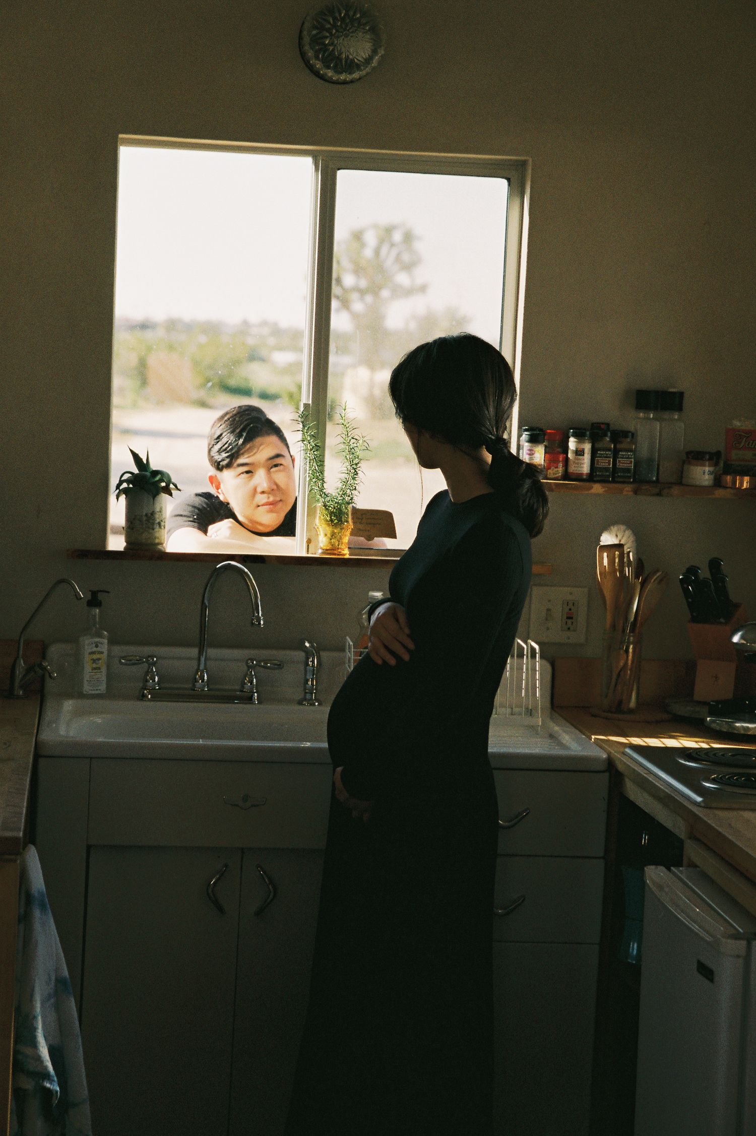 Sunlit kitchen interior with person standing by window and sink.