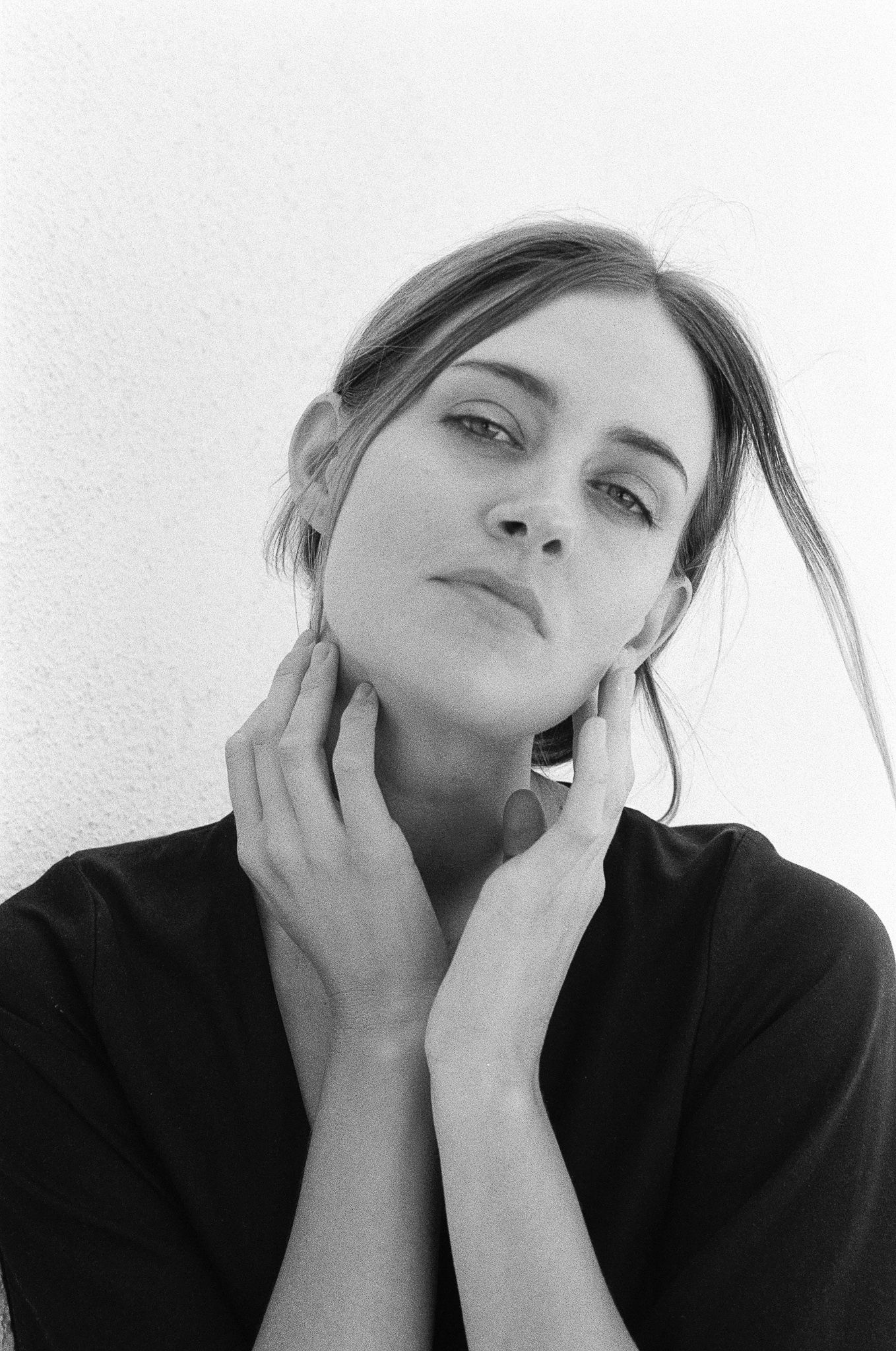 Black and white artistic portrait showing contemplative pose against plain wall.