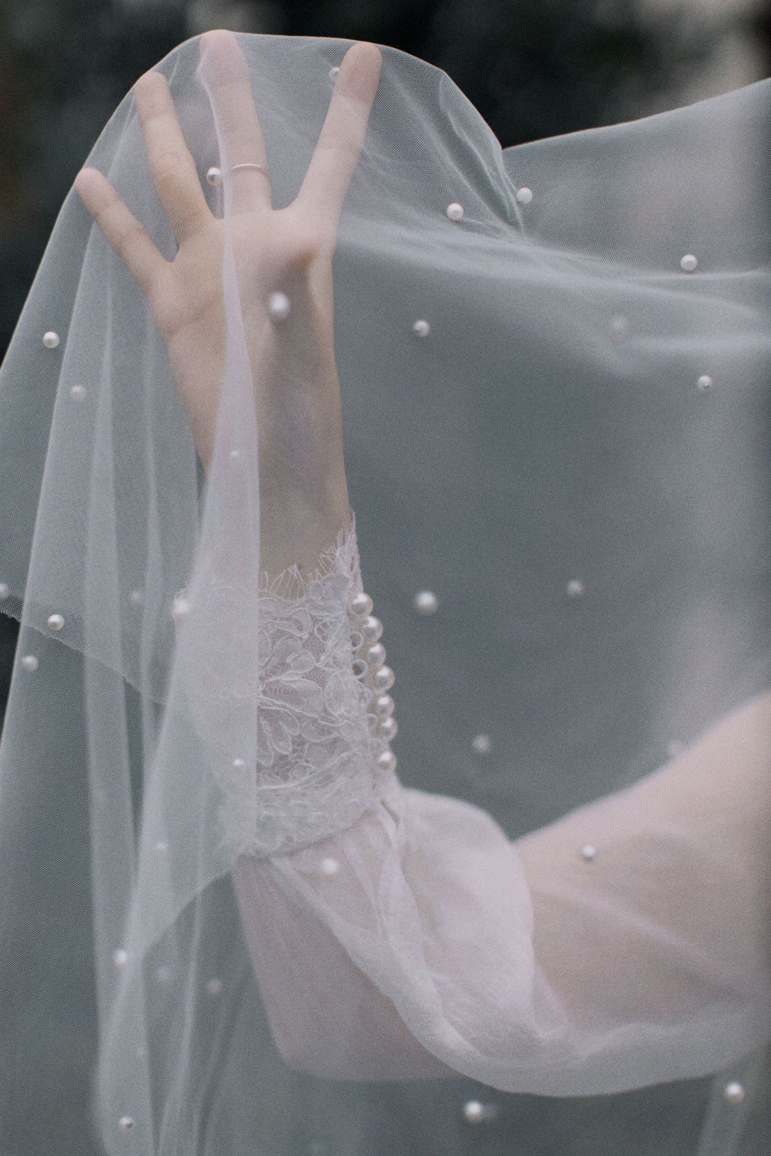 A delicate white bridal veil with pearl embellishments flows ethereally in soft light.