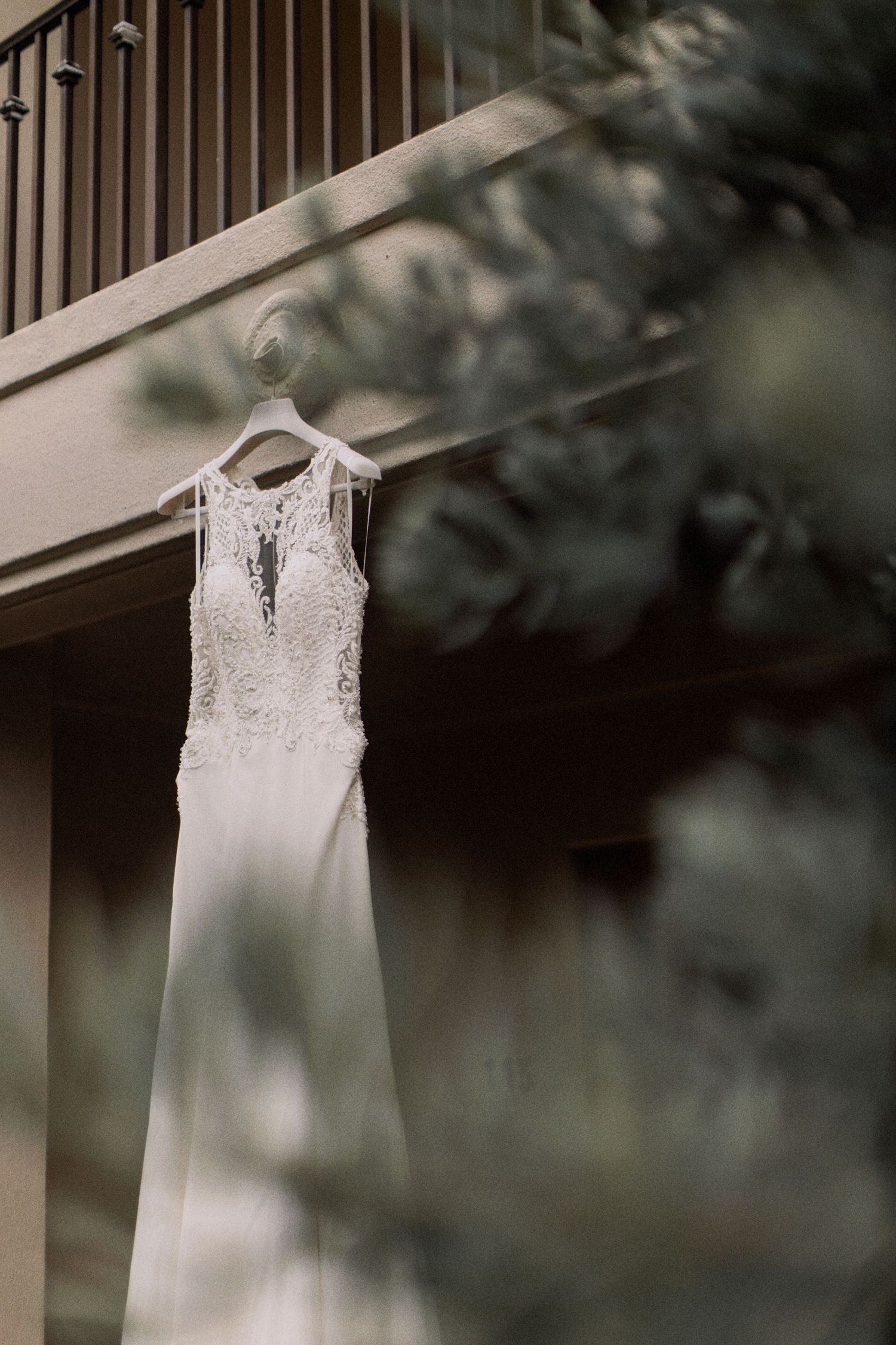 White lace wedding dress hanging elegantly against a blurred outdoor background.