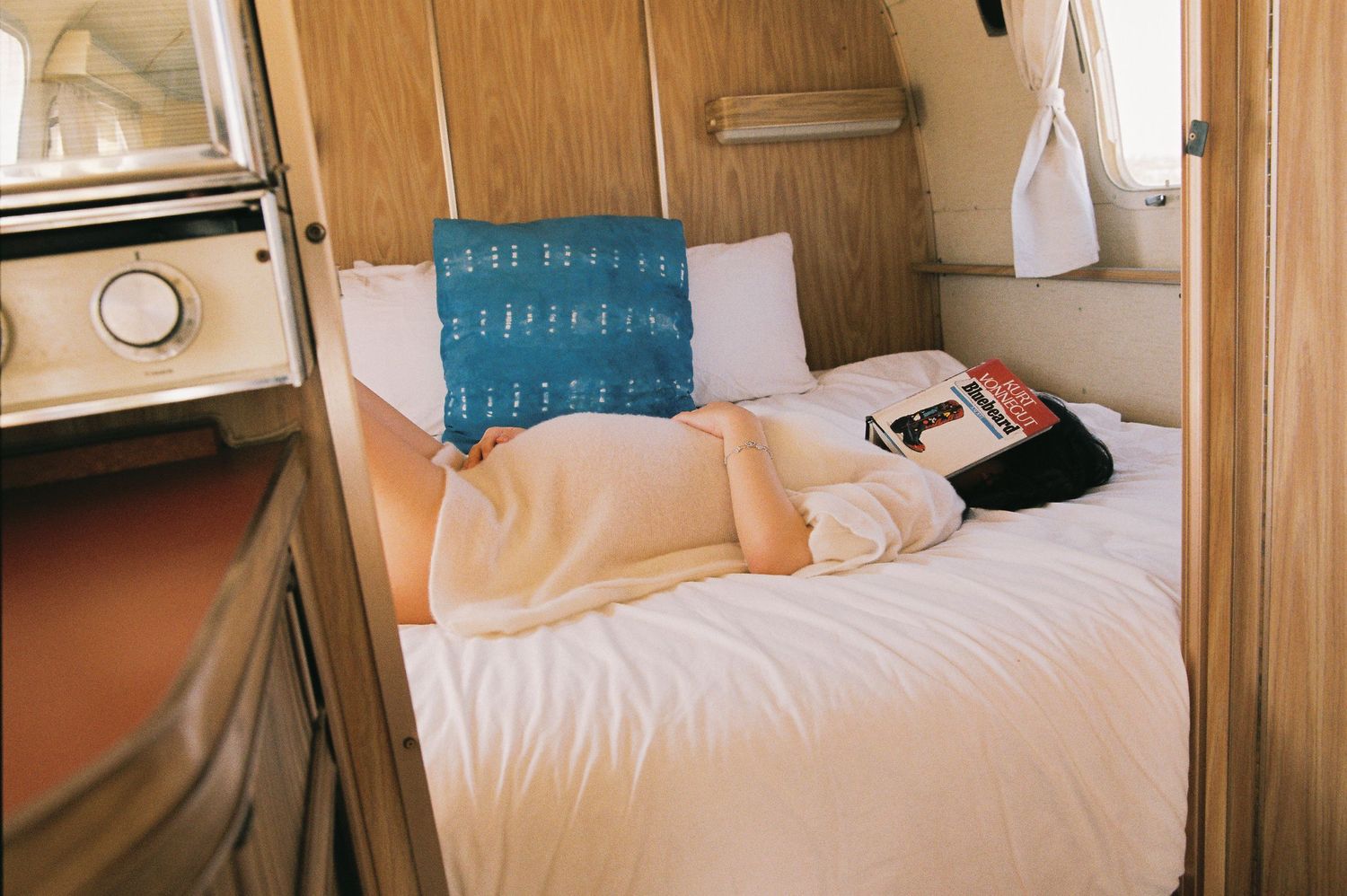 Interior view of cozy camper van bed with blue pillow and natural lighting.