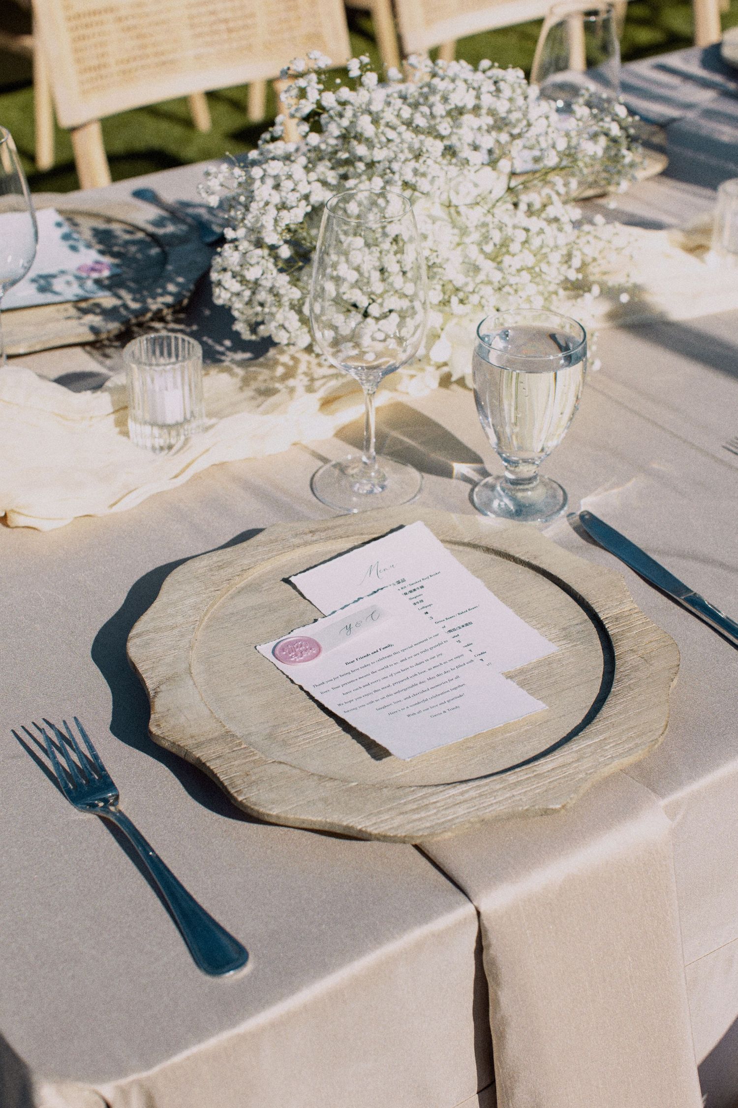 Elegant wedding place setting with baby's breath centerpiece, glass goblet, and menu card on a white tablecloth.