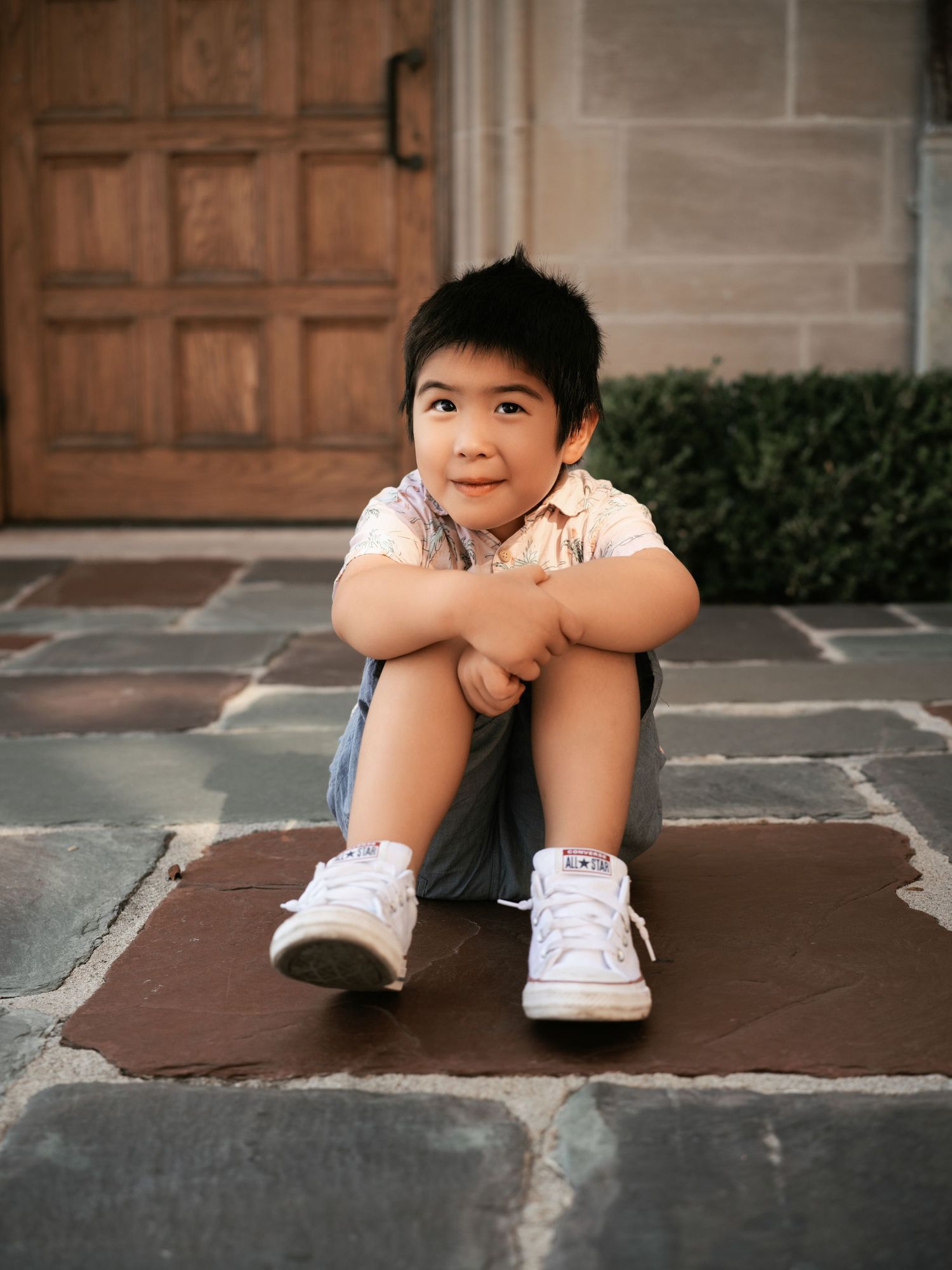 A young child sits casually on stone steps wearing white sneakers.