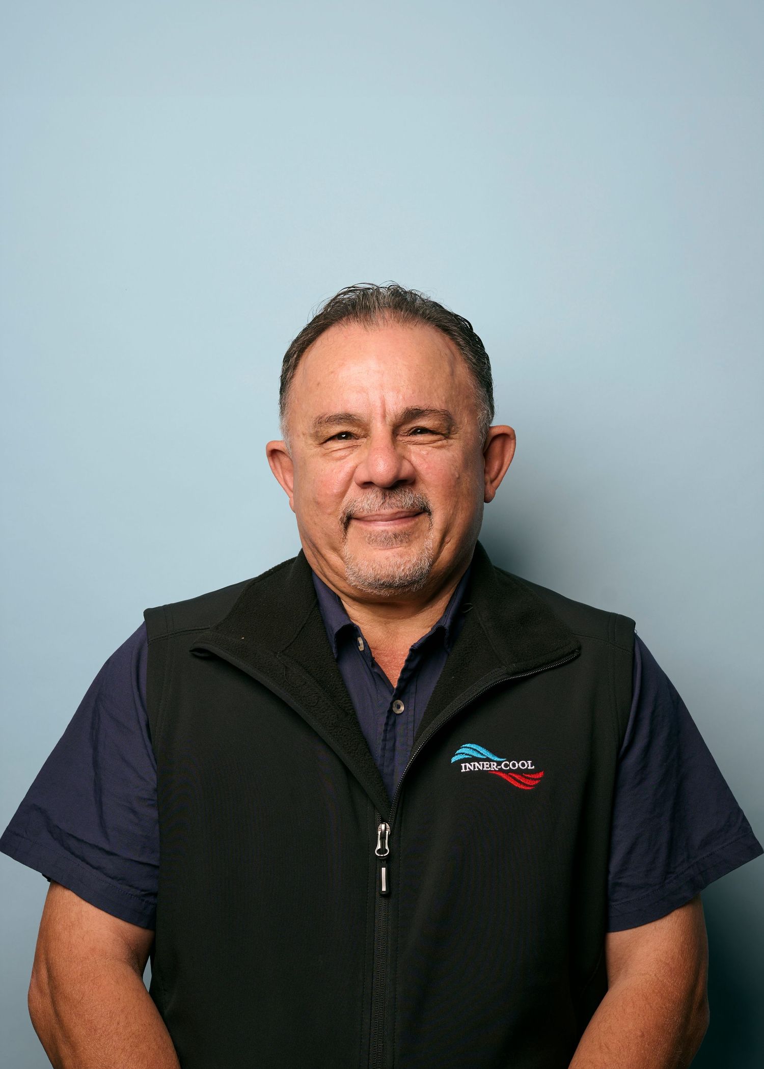Four headshots of a person wearing a navy polo and black vest against a light blue background.