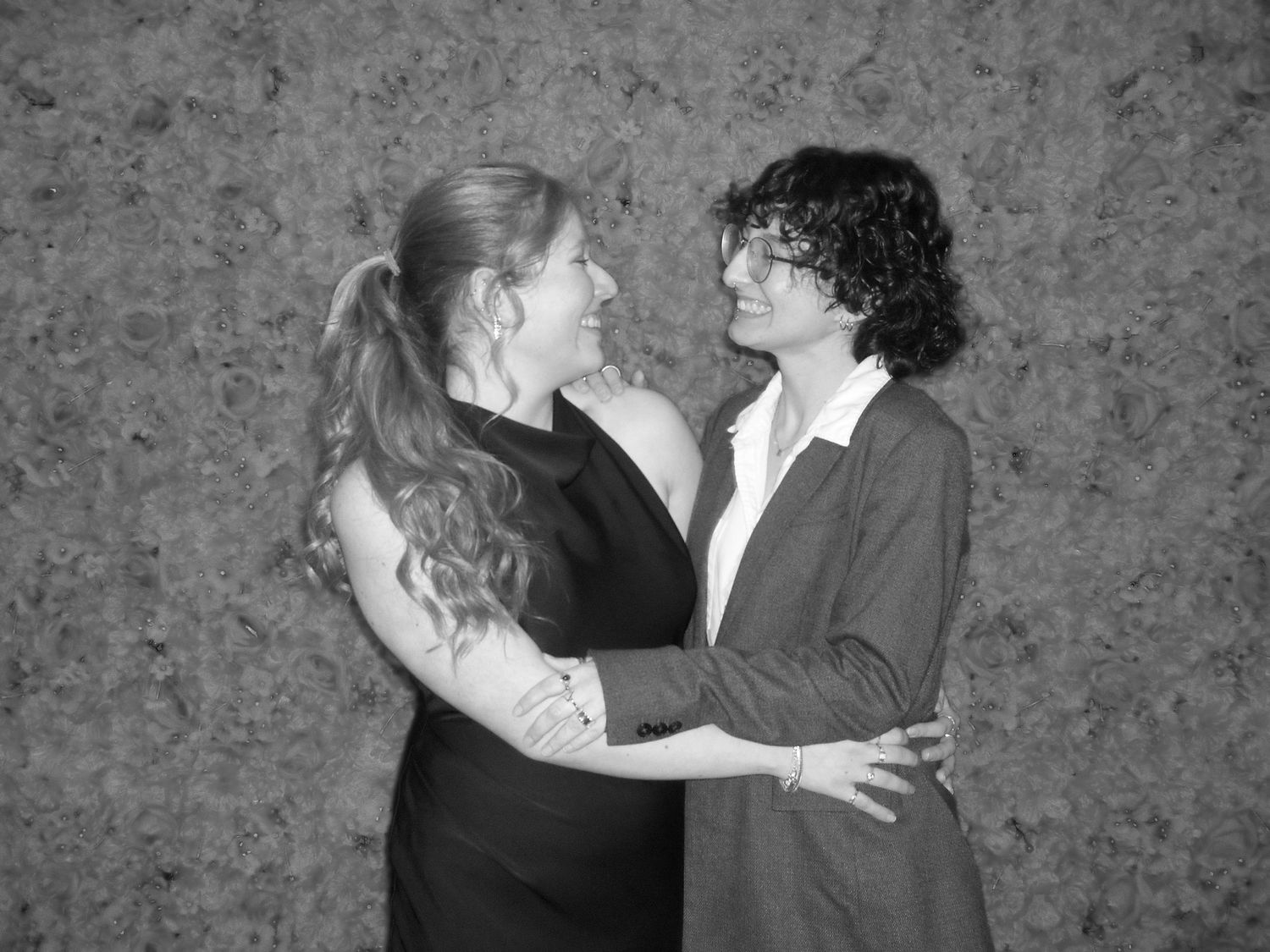 Two people in black and white attire embrace in an intimate moment against a textured backdrop.