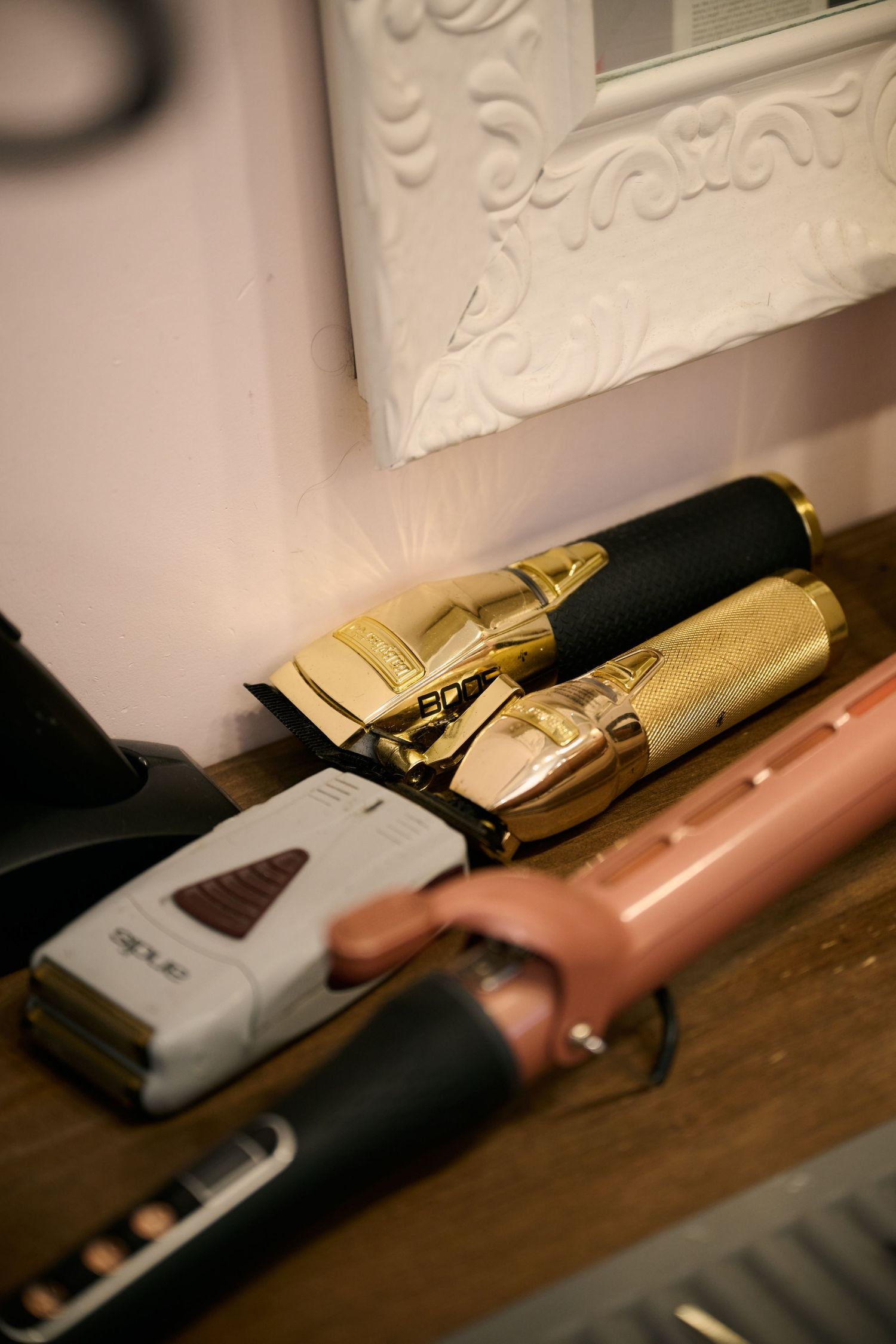 Close-up shot of professional hair styling tools including gold clippers and pastel colored accessories on wooden surface.