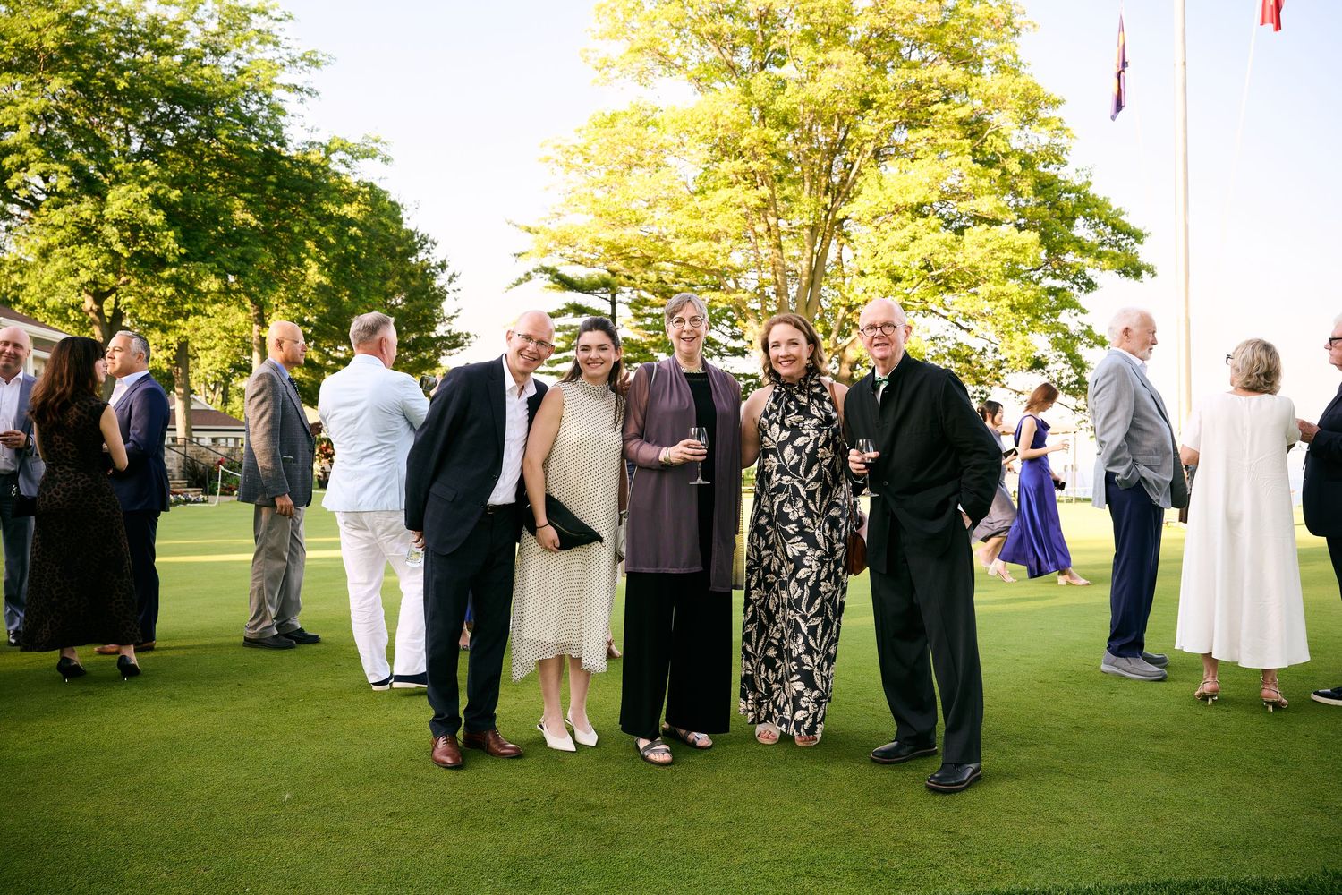 Elegantly dressed guests mingling outdoors on a green lawn at a formal garden party event.