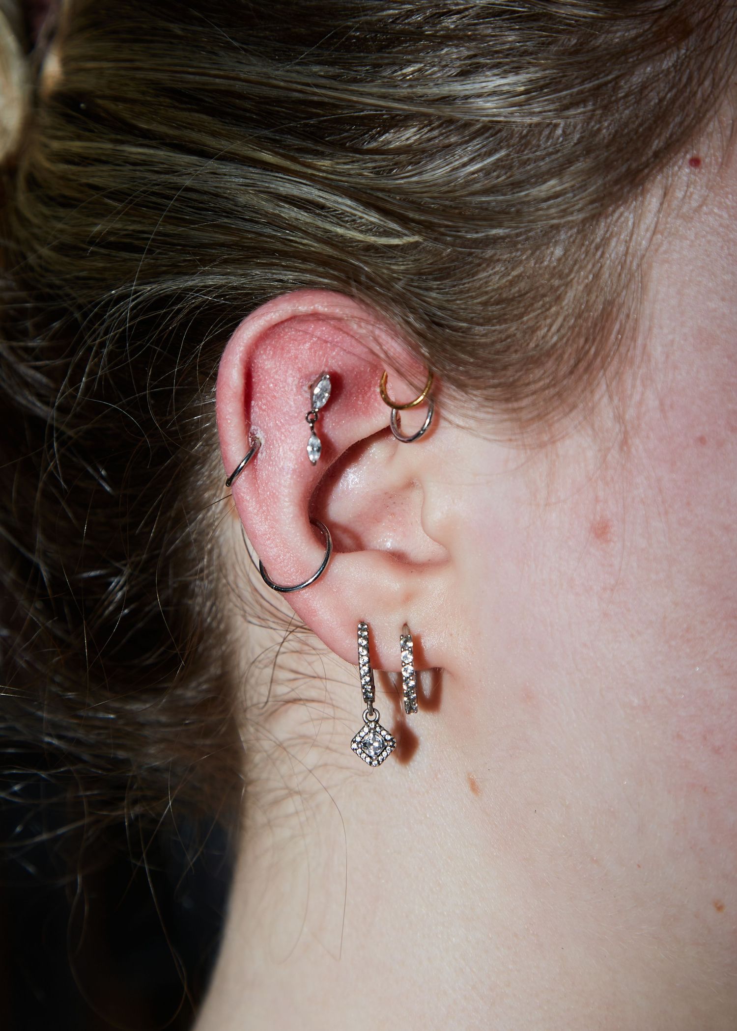 Close-up of multiple piercings and jewelry decorating an ear.