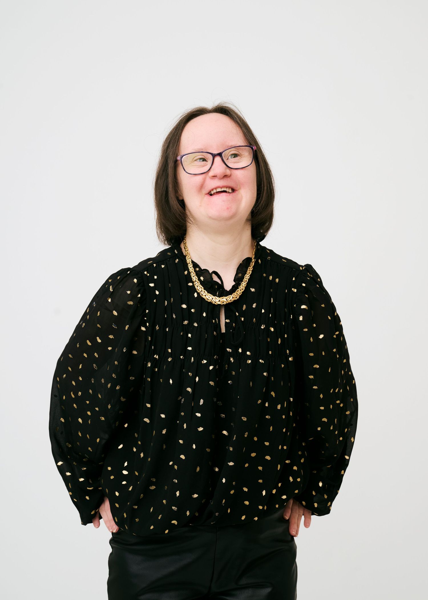 A model in a black dress with gold speckles poses confidently against a white background.