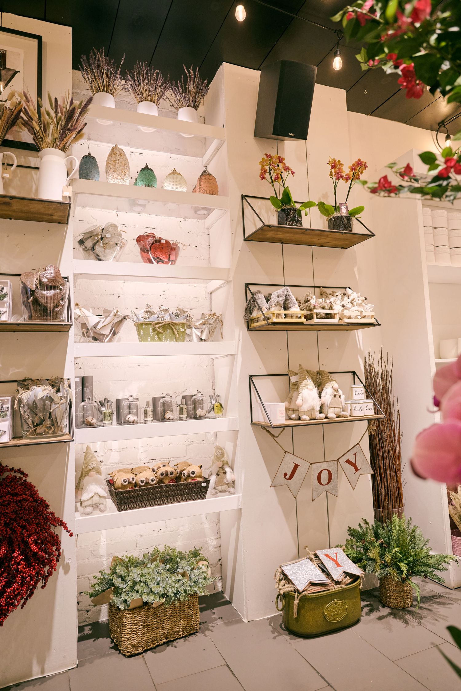 White shelving display with potted plants, decorative items and love banner in a boutique setting.