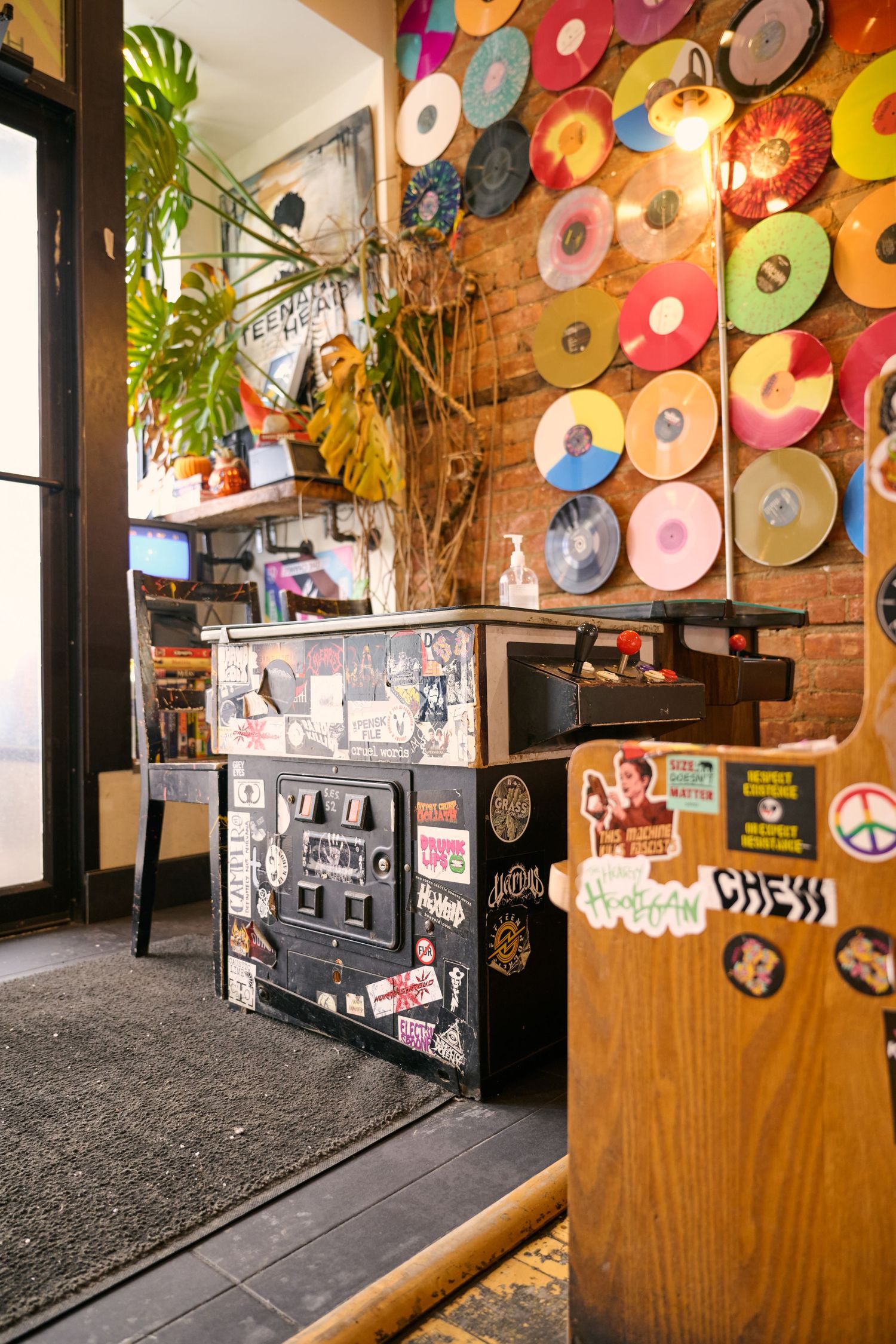 Vibrant vinyl records decorate a brick wall in a cozy cafe interior with plants and vintage decor.