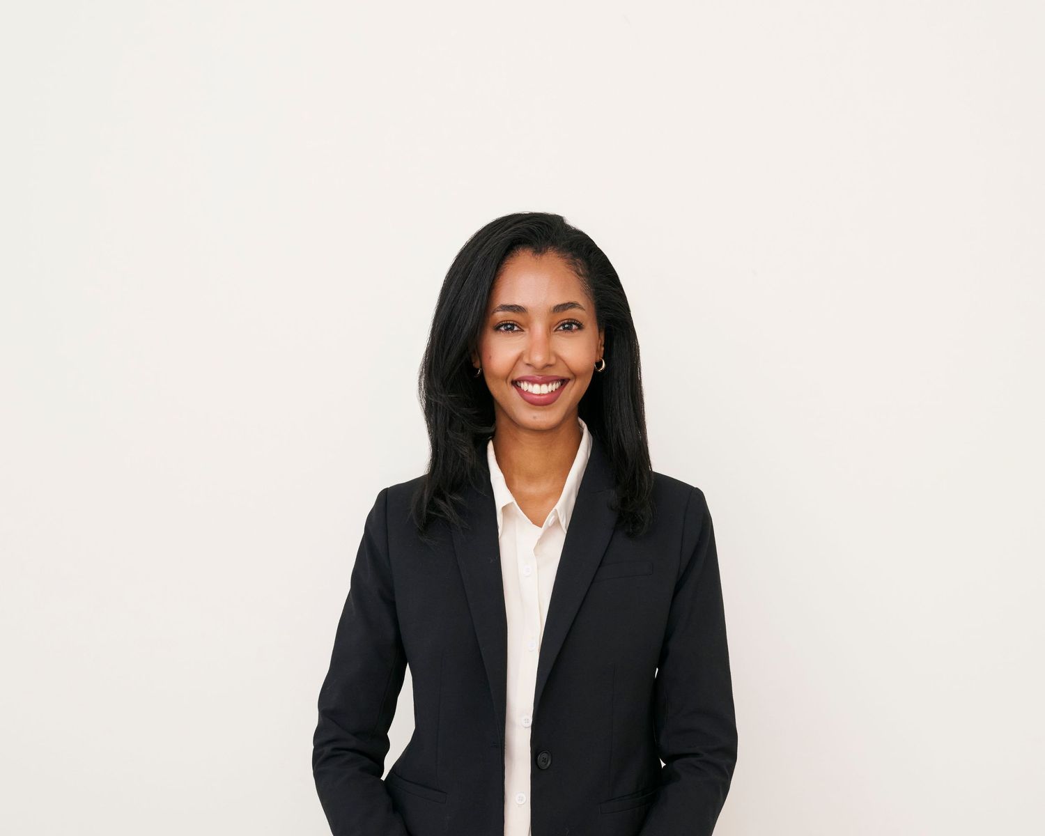 Professional in a black blazer and white blouse smiles warmly against a white background.