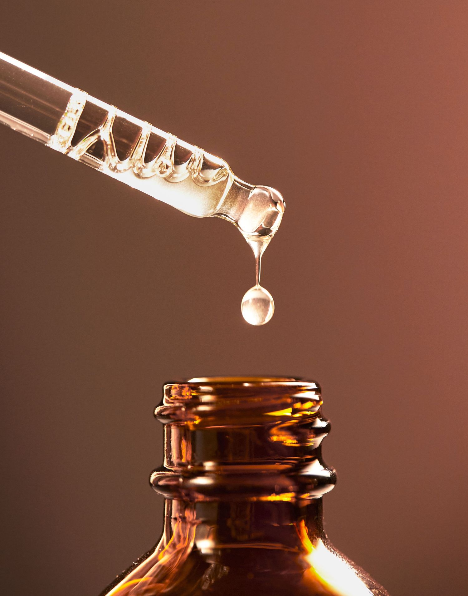 Clear liquid dropping from a dropper into an amber glass bottle.