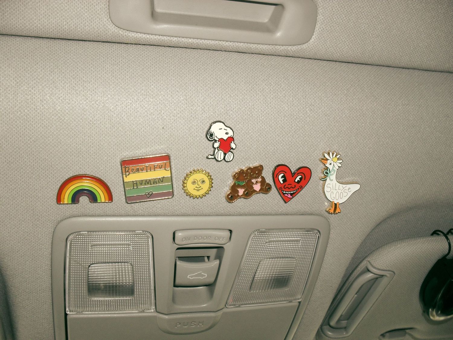 Colorful stickers including a rainbow, pride flag, smiley face, teddy bear, heart, and goose decorating a car's ceiling interior.