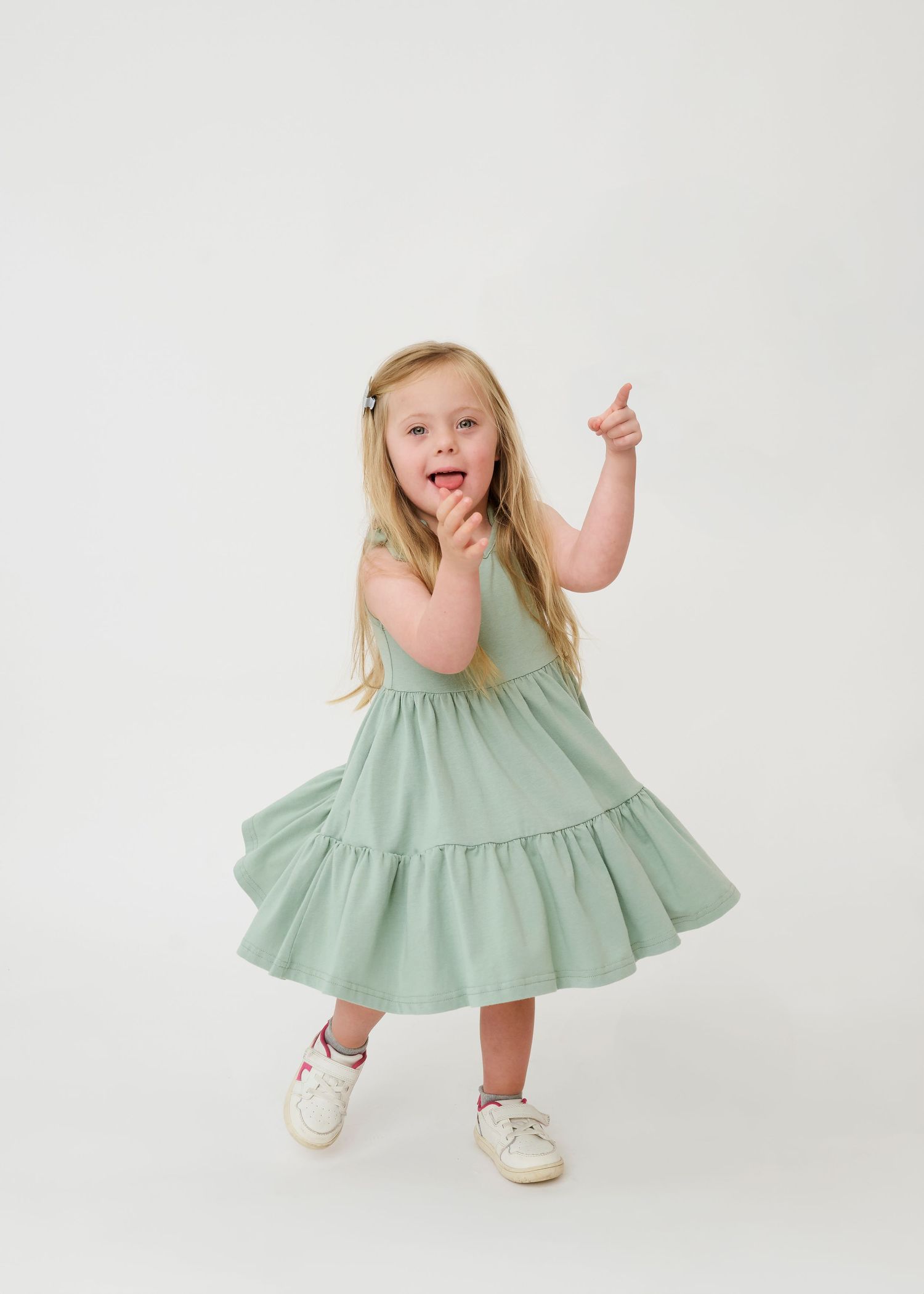 A child in a mint green dress twirls and dances playfully against a white background in a three-photo sequence.