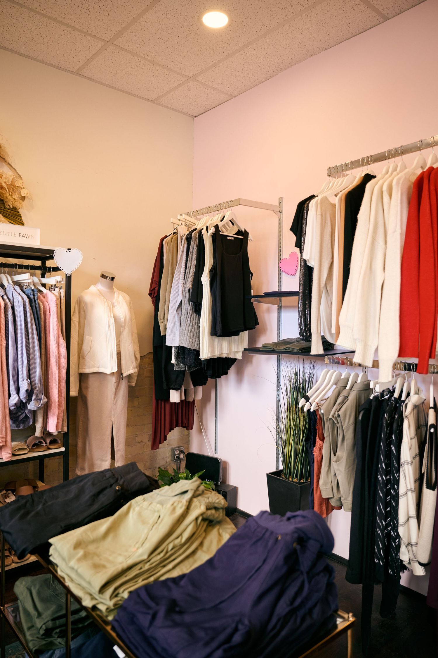 A clothing store interior displays racks of white, black and red garments with folded clothes on shelves below.