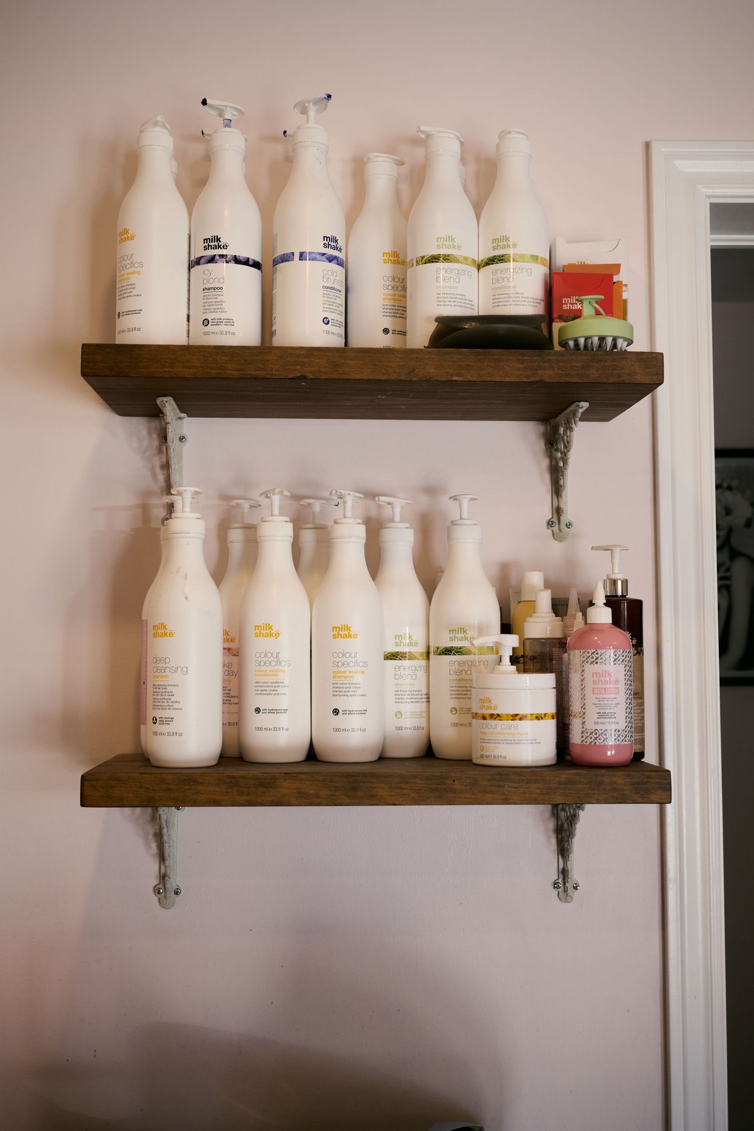 Rustic wooden shelves display a collection of white glass milk bottles and toiletries against a pale wall.