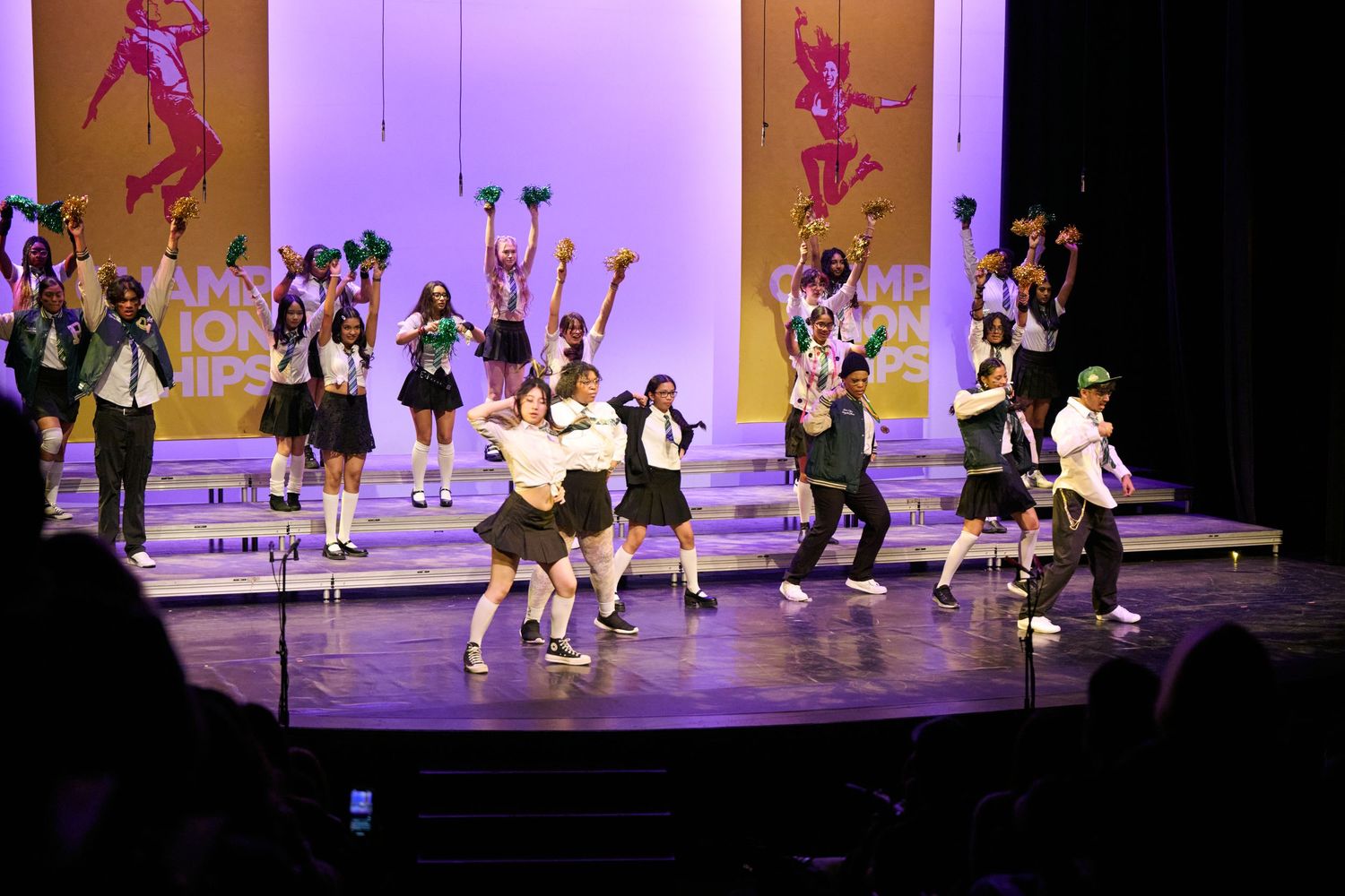 Dancers perform a choreographed routine on a stage with pink and purple lighting during a dance recital.