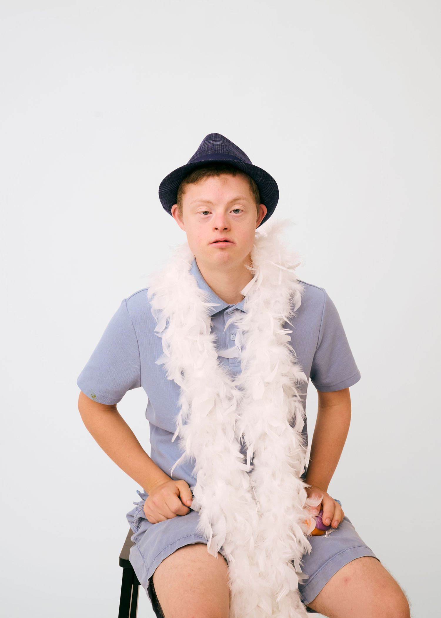 A person wearing a gray shirt and hat poses playfully with a white feather boa in a series of four studio shots.