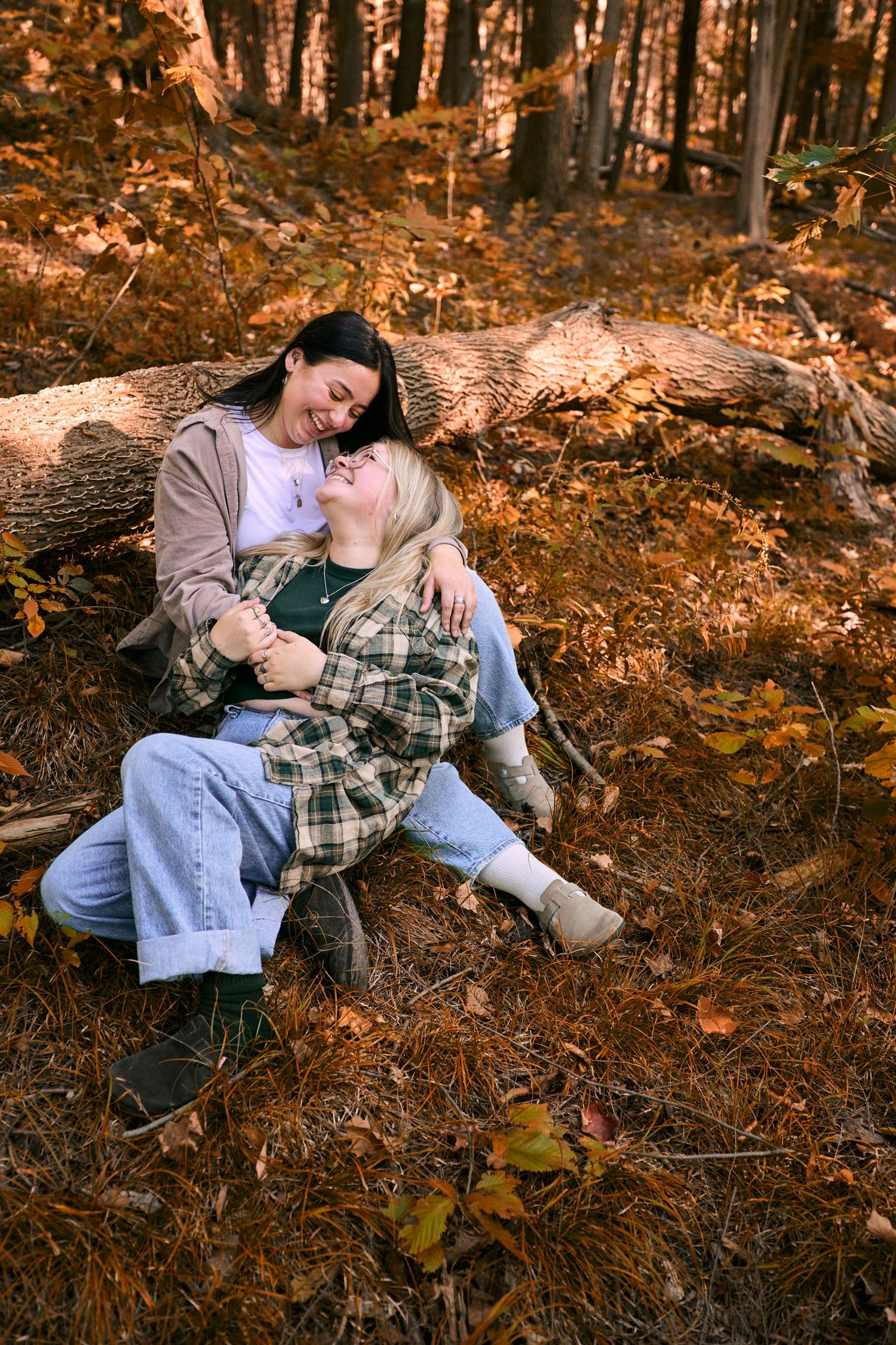 Couple sharing intimate moments while laying on autumn leaves in a wooded setting.