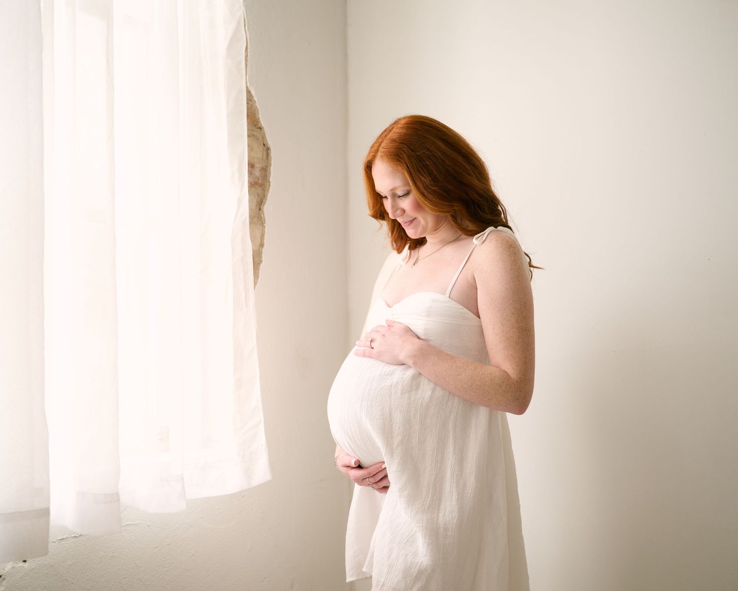 A series of ethereal white photos showing a woman in flowing fabric by a bright window.