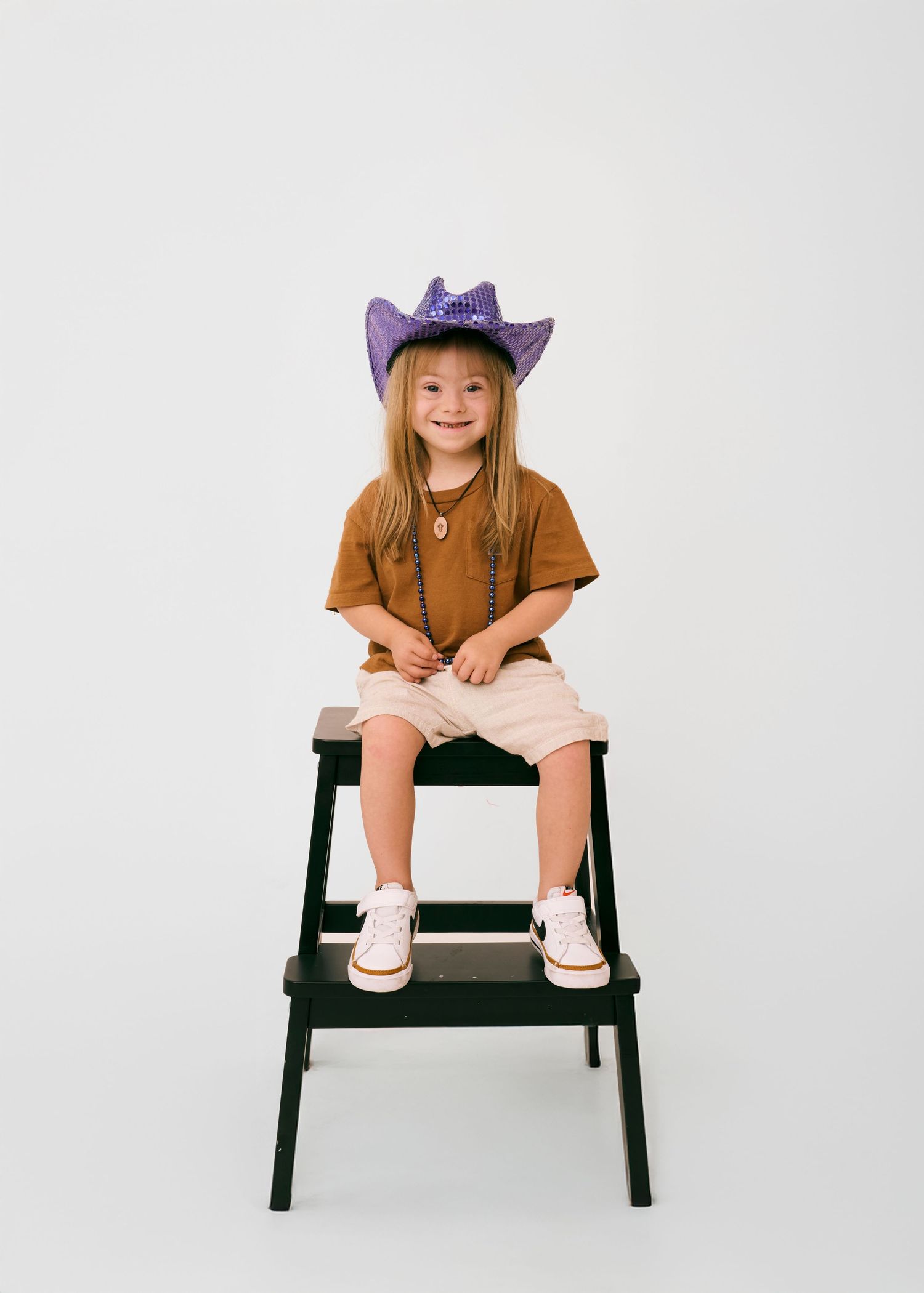 A child in a cowboy hat and brown shirt sits on a black bench in four sequential poses against a white background.
