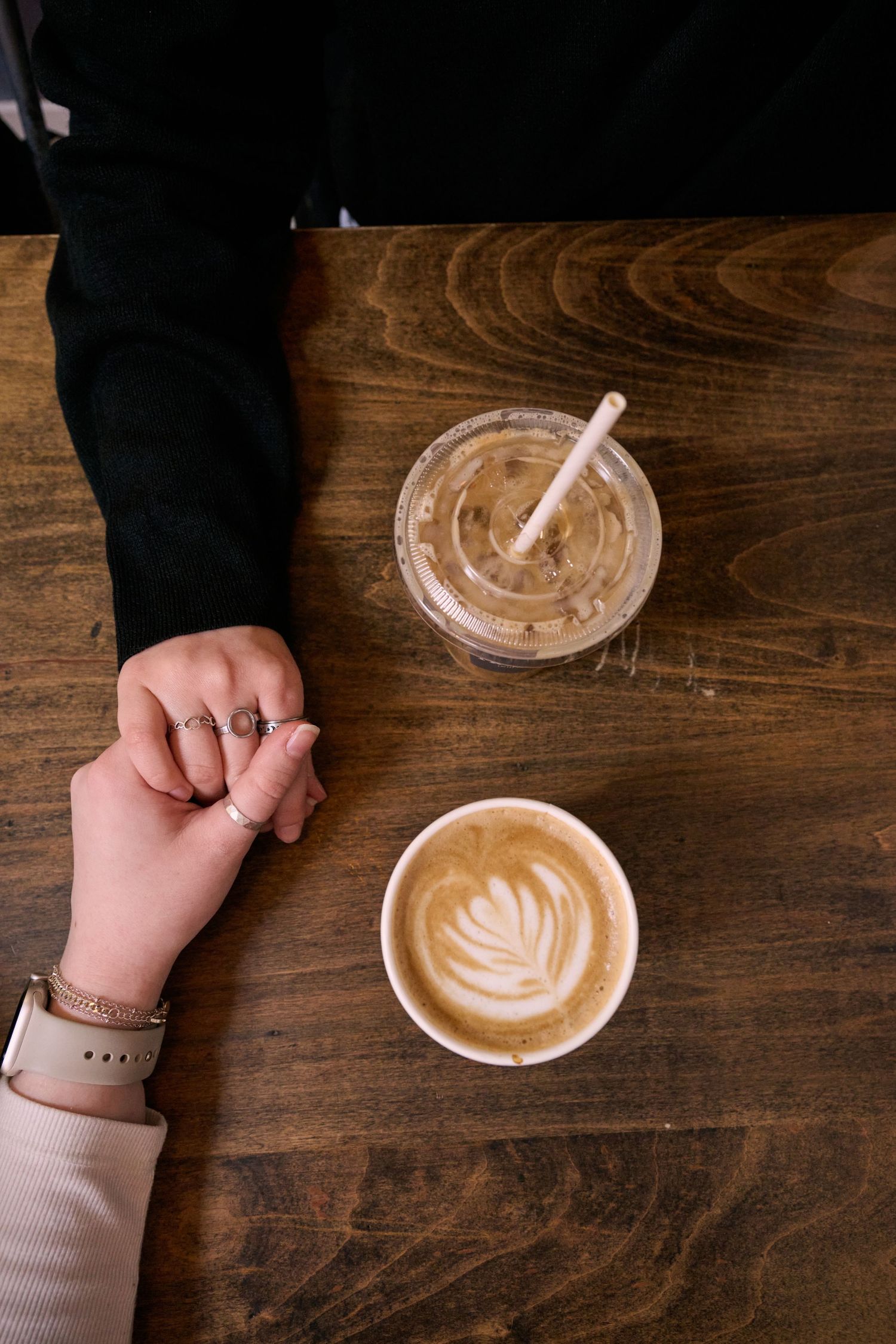 Overhead view of two coffee drinks on wooden table with latte art and iced coffee with straw.