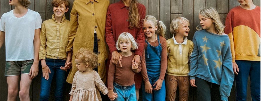 A large group of people wearing vintage 1970s style clothing stand together in a casual formation.