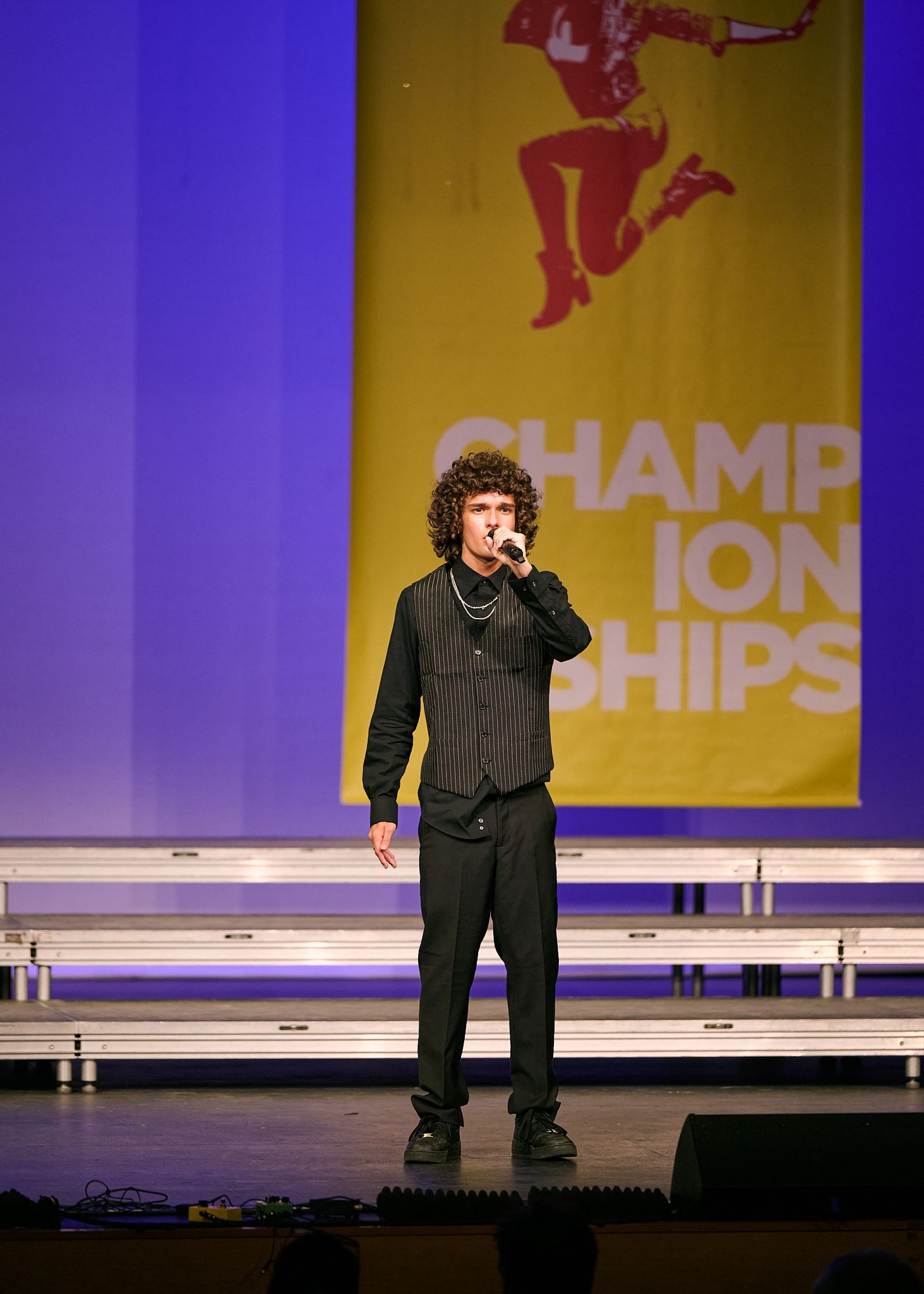 Young performer singing into microphone on stage at a Championships event with purple backdrop.